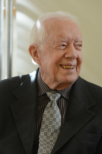 Former President Carter, smiling, wearing a black suit and a dazzling striped tie.