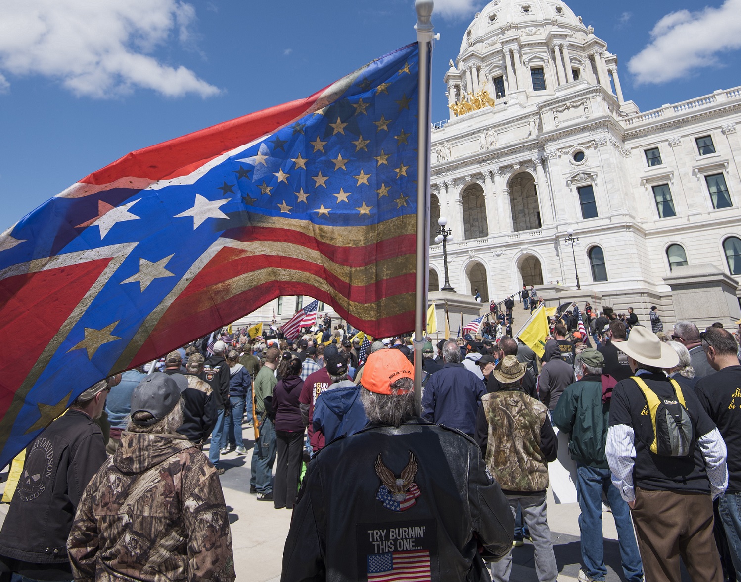 A crowd of people , one of whom carries a large flag merging the Confederate flag and the American flag into a single design.