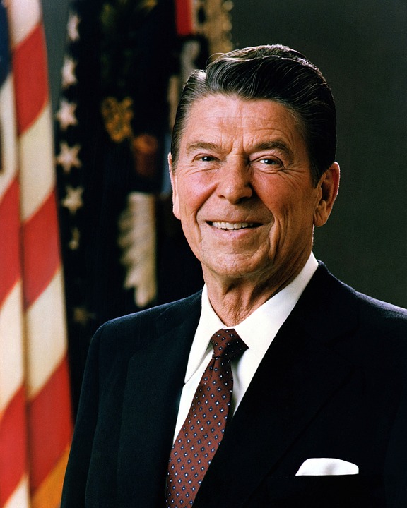Portrait of Ronald Reagan, cheerfully posing in front of an American flag.