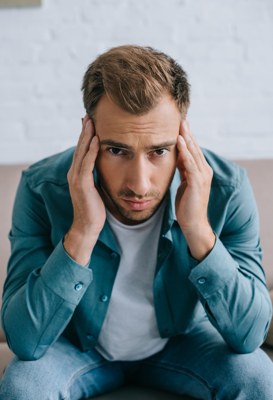 Young man with headache looking at camera at home - depositphotos.com