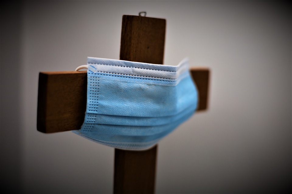 A blue disposable face mask looped around a wooden cross.