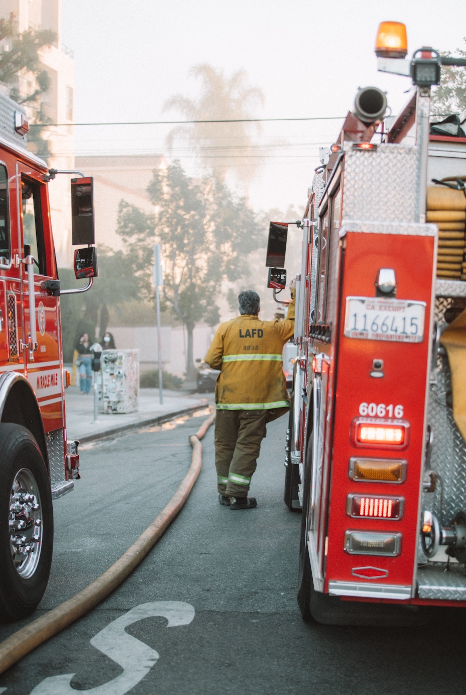 LAFD firefighter with hose and trucks; image by Spencer Davis, via Unsplash.com.