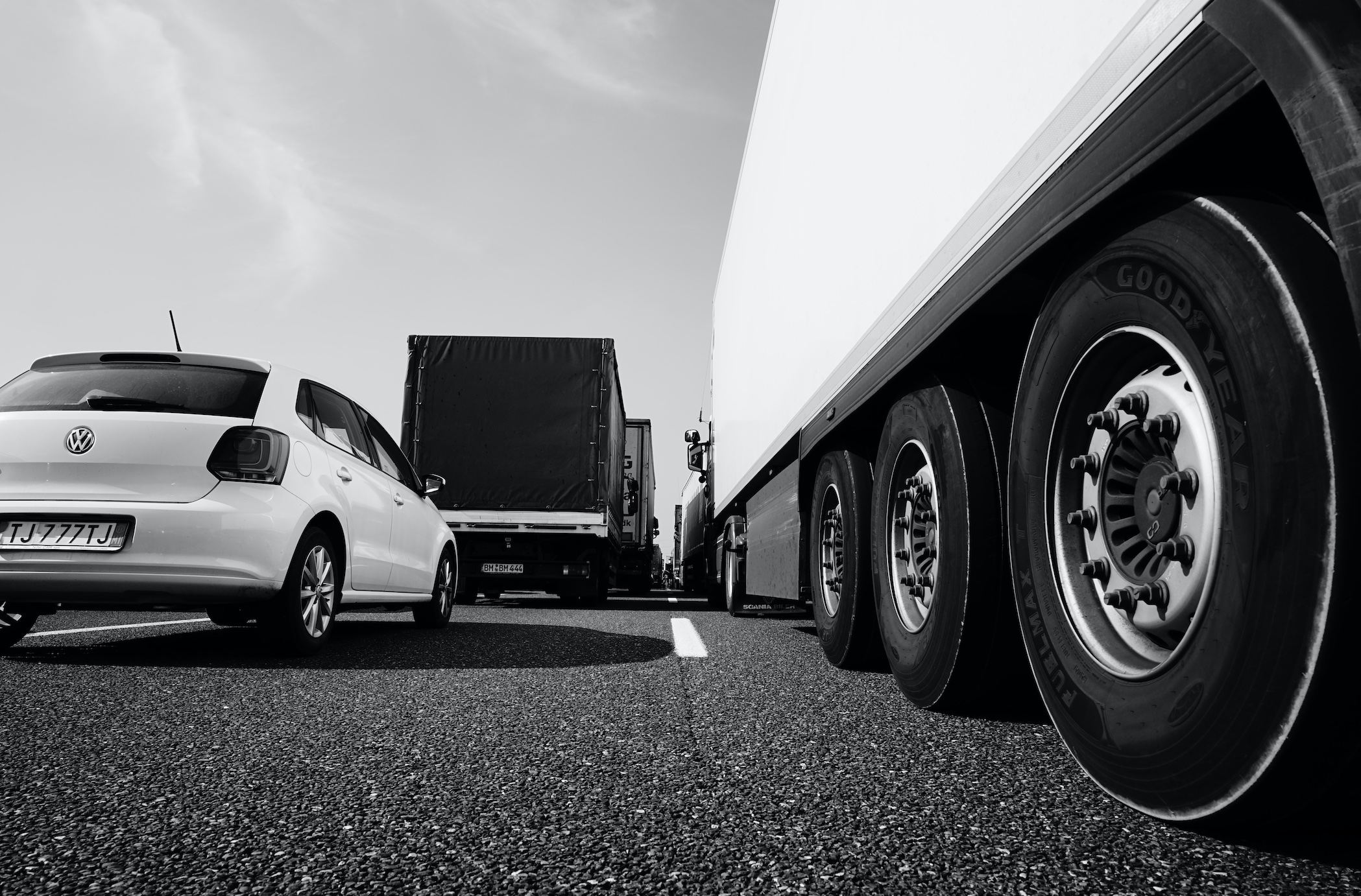 Black and white photo of semi-truck stuck in traffic jam, taken at wheel height; image by Wolfgang Hasselmann, via Unsplash.com.