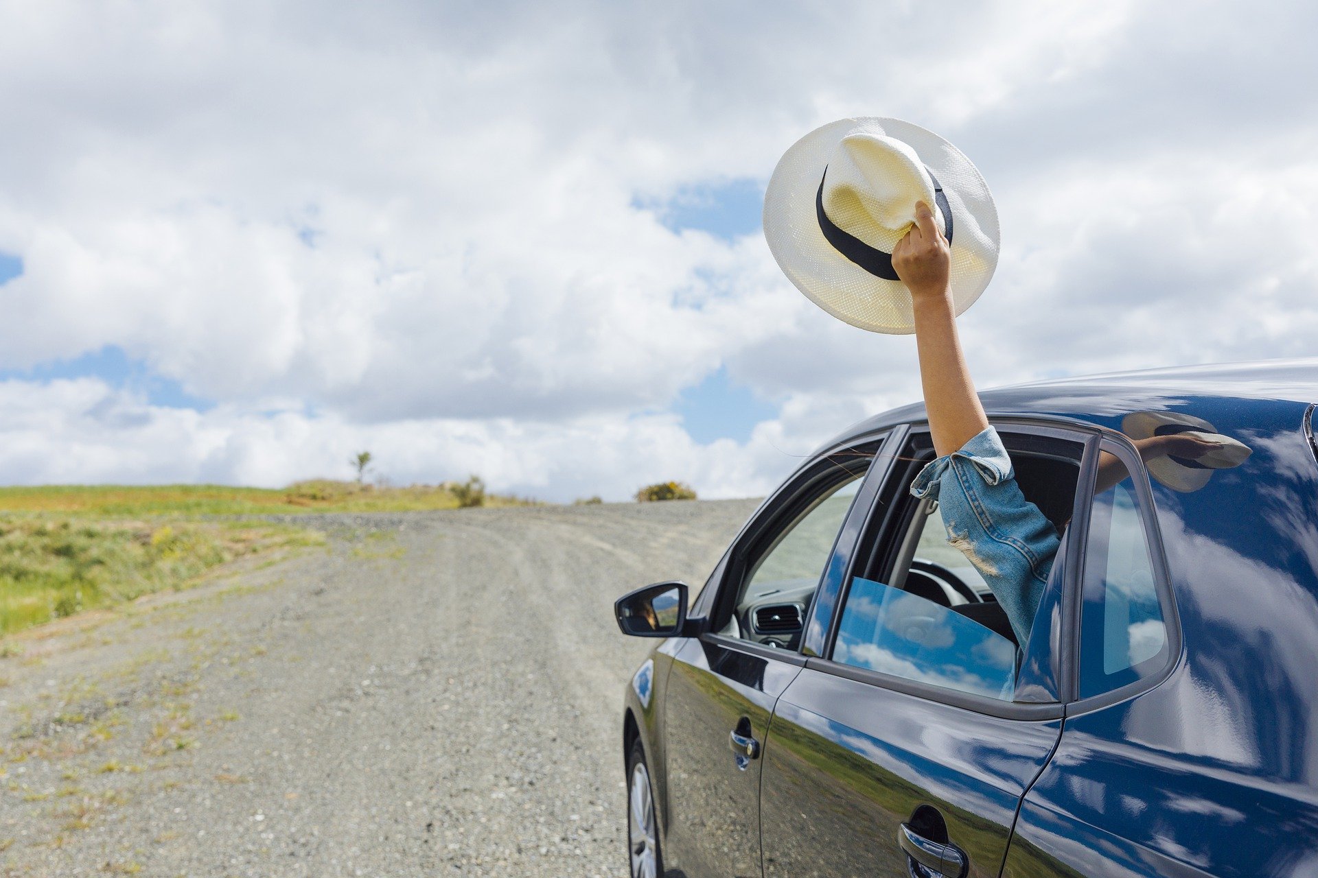 Car driving down dirt road, woman waving hat from rear window; image by Tekhnika, via Pixabay.com