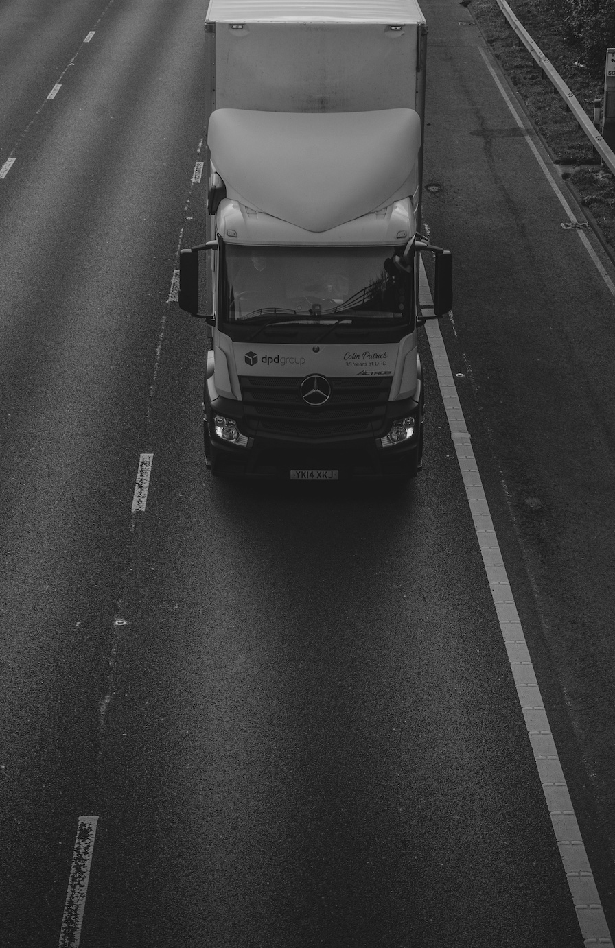 Grey scale semi-truck driving toward viewer; image by Dominic Egginton, via Unsplash.com.