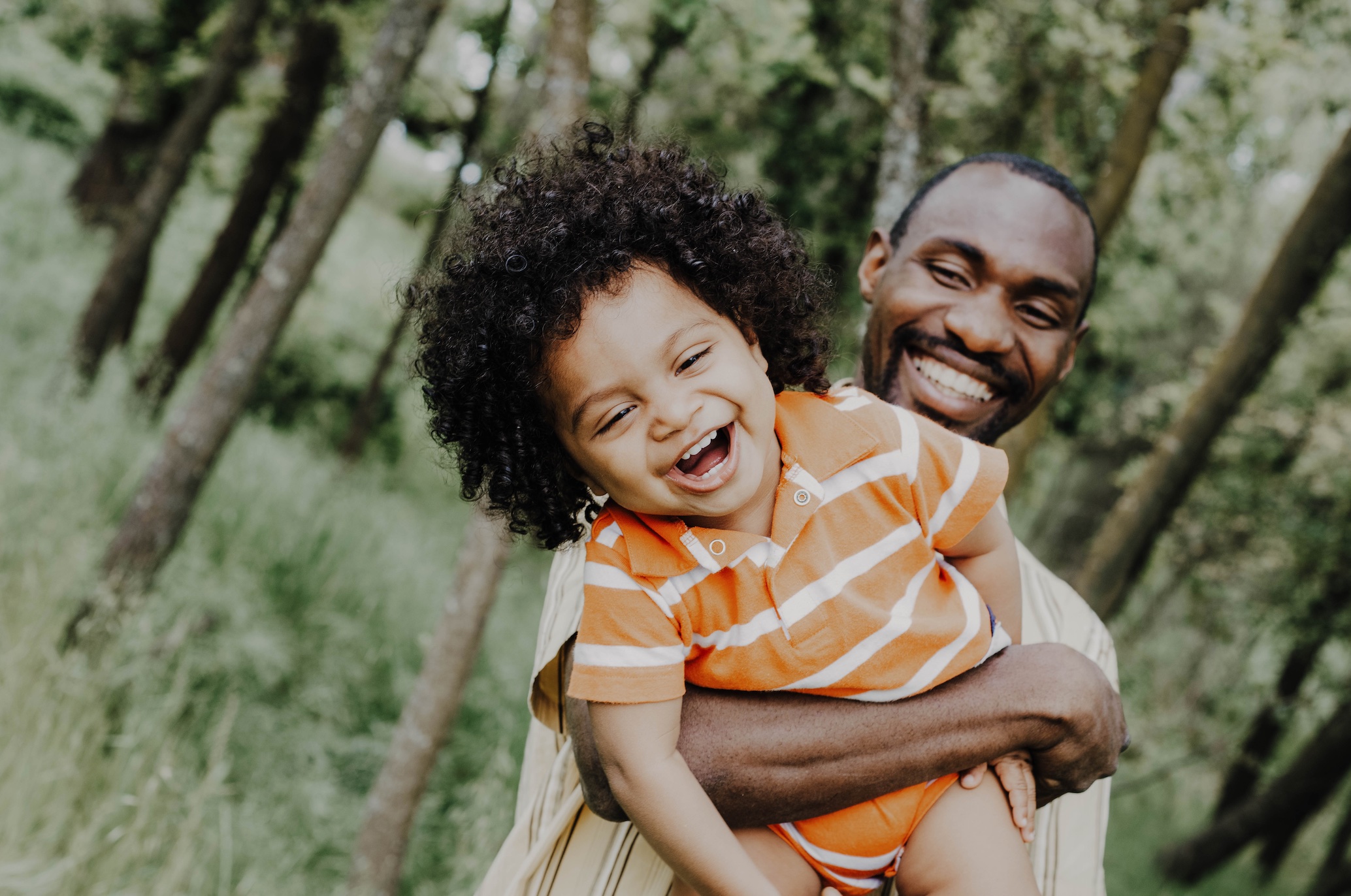 Laughing child in father's arms; image by Joice Kelly, via Unsplash.com.