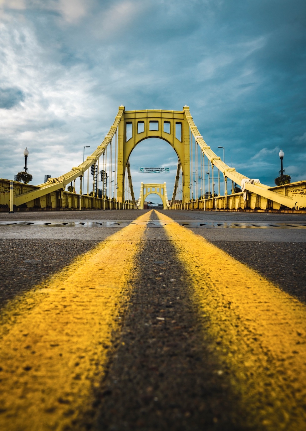 Pavement-level view of double yellow lines on a bridge in Pittsburgh, PA; image by Dylan Sauerwein, via Unsplash.com.