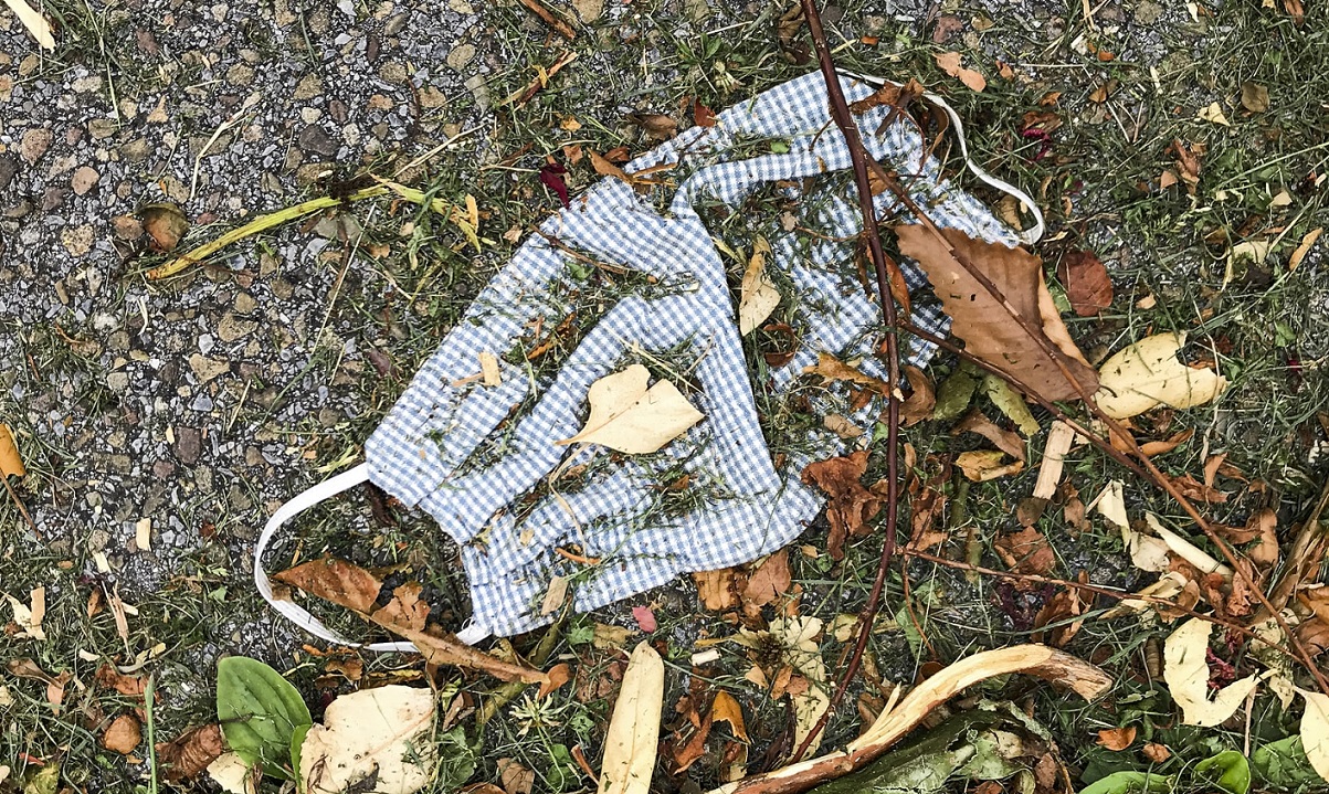 A used cloth face mask discarded on the ground and covered with dirt and dried leaves.