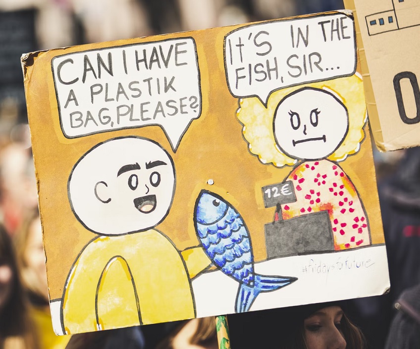 Protest sign depicting retail scene with a customer asking for a plastic bag, being told that it's already in his fish.