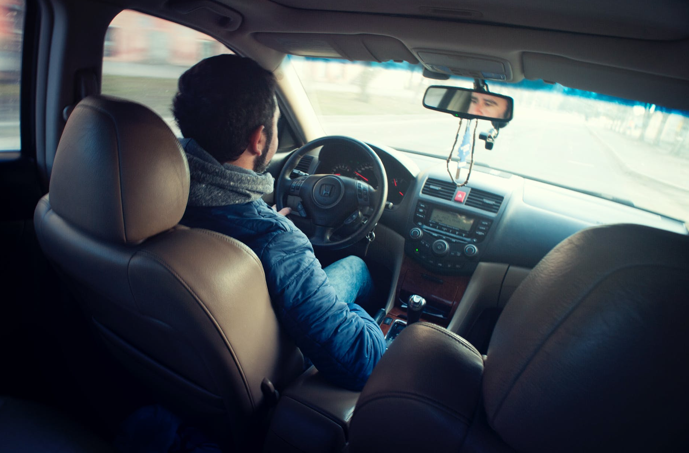 Man in blue jacket driving car; image by Alexandr Podvalny, via Pexels.com.