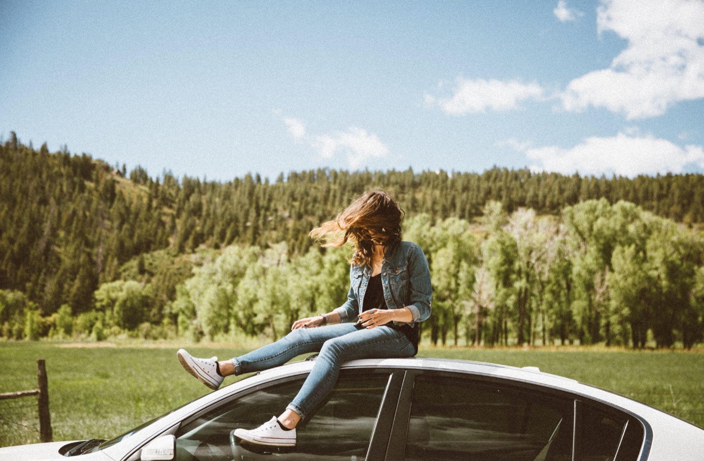 Teen girl sitting on top of car; image by Averie Woodard, via Unsplash.com.