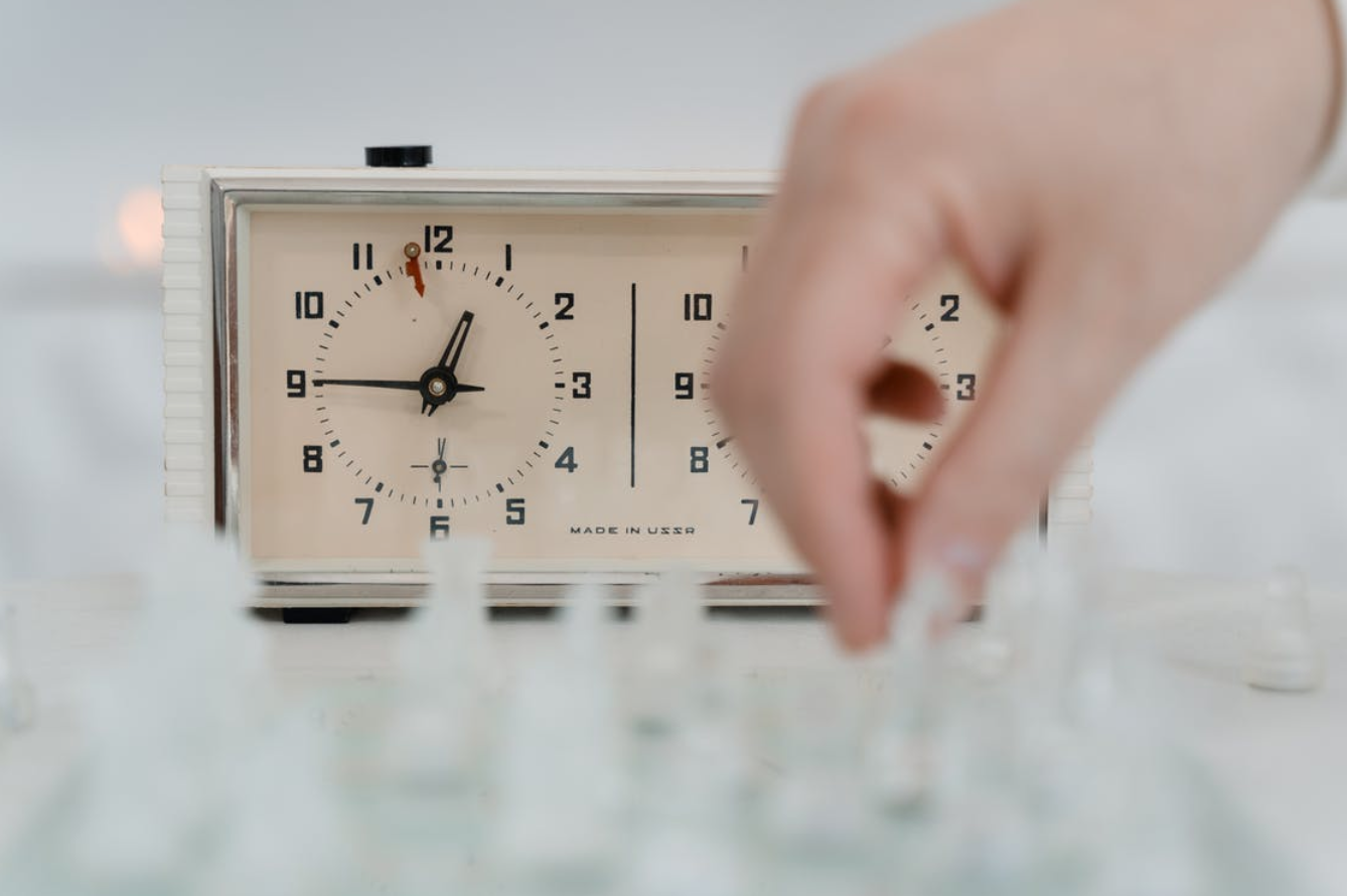 Clock with blurred image of hand; image by Tima Miroshnichenko, via Pexels.com.