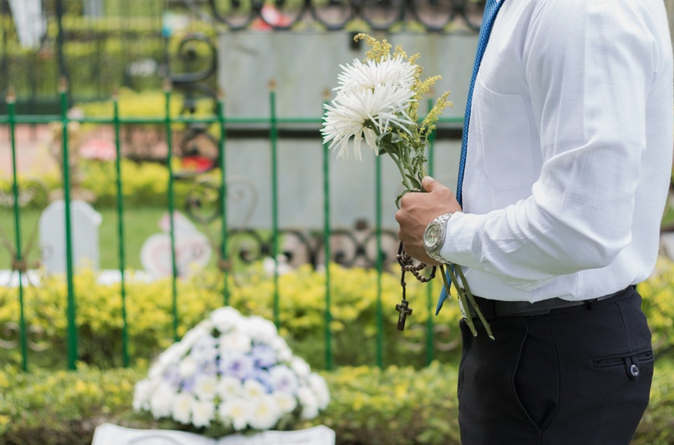 Man at funeral, holding flowers; image by Joaph, via Pixabay.com.