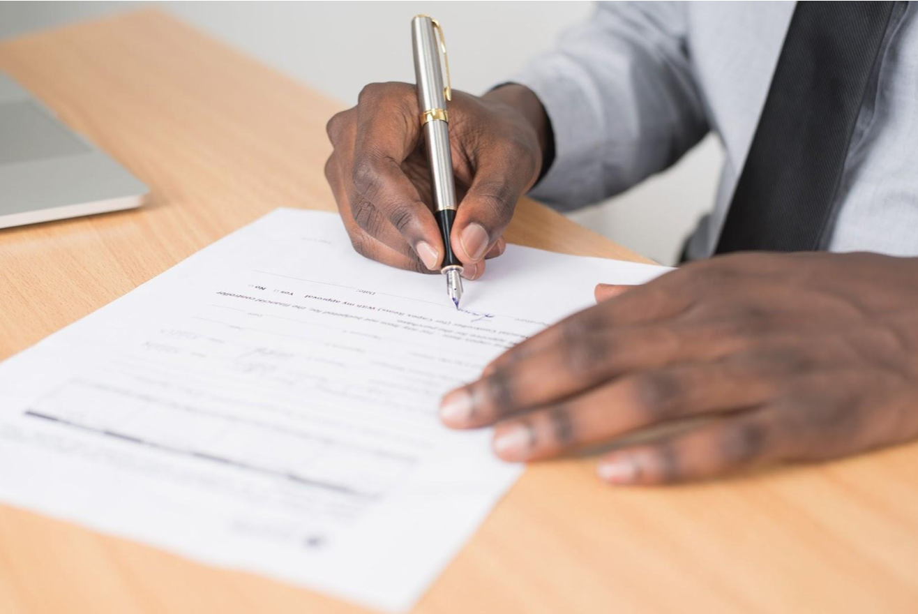 Person holding a grey twist pen and signing a white piece of paper.