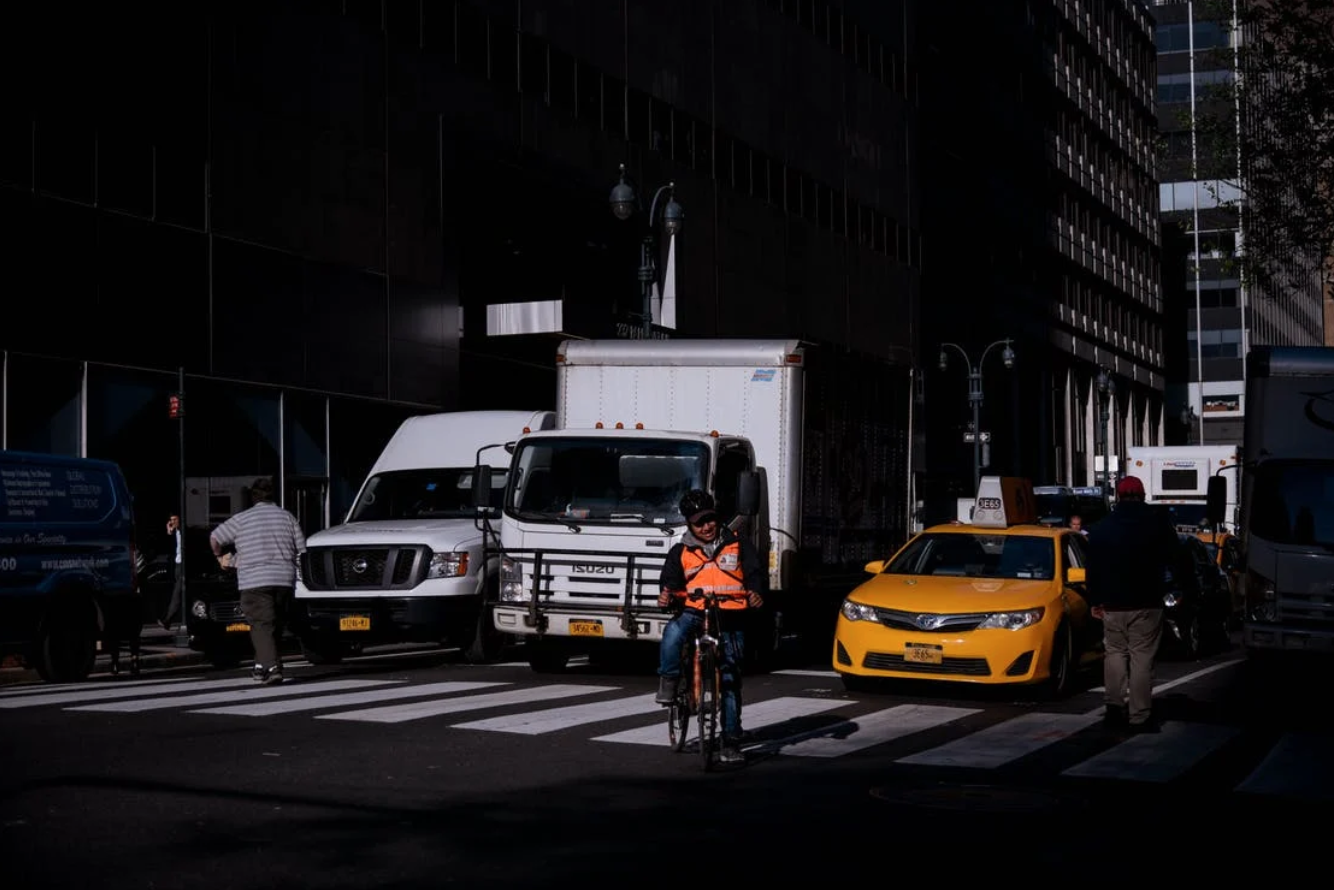 People Walking on Pedestrian Lane in Front of Vehicles; image by gdtography, via Pexels.com.