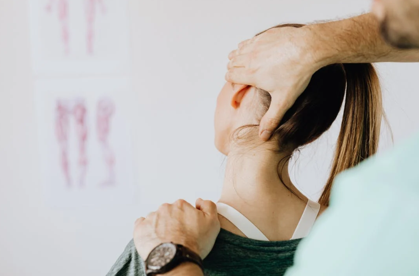 Professional massage therapist treating woman's injured neck; image by Karolina Grabowska, via Pexels.com.