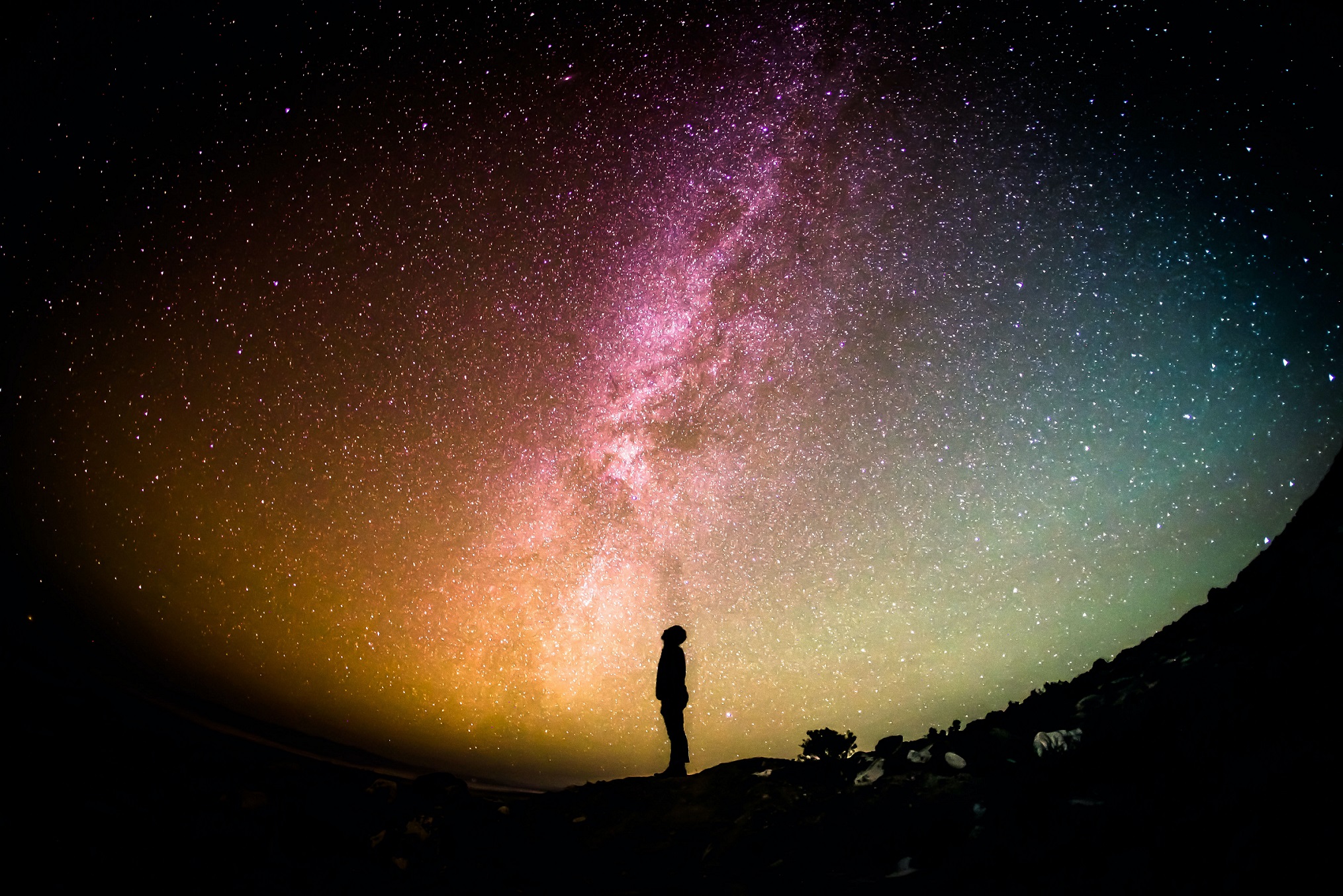 A lone human figure in shadow against the vast, star-filled night sky.