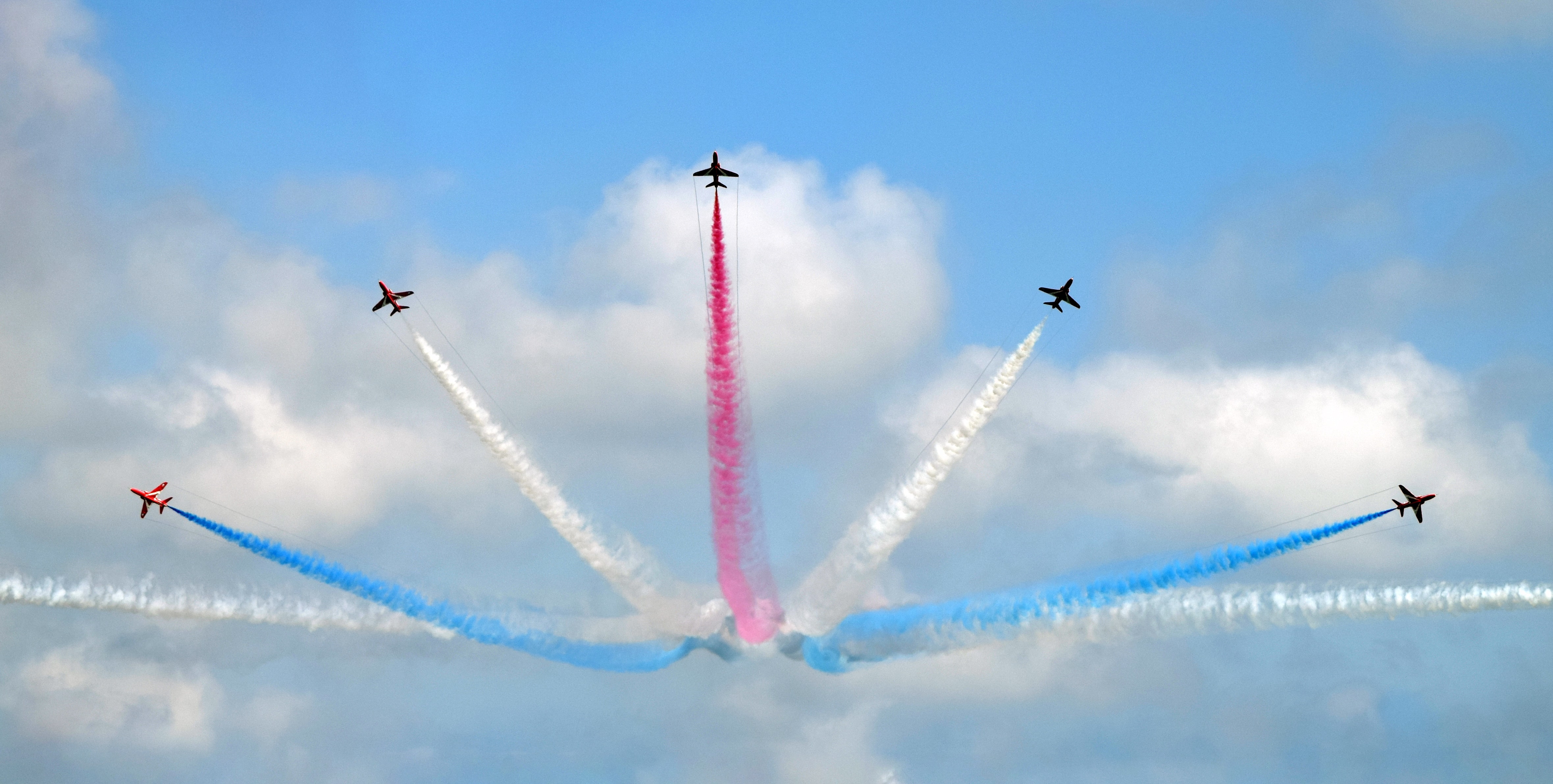 Jets creating concentric smoke trails in red, white, and blue; image by Owen Kemp, via Unsplash.com.