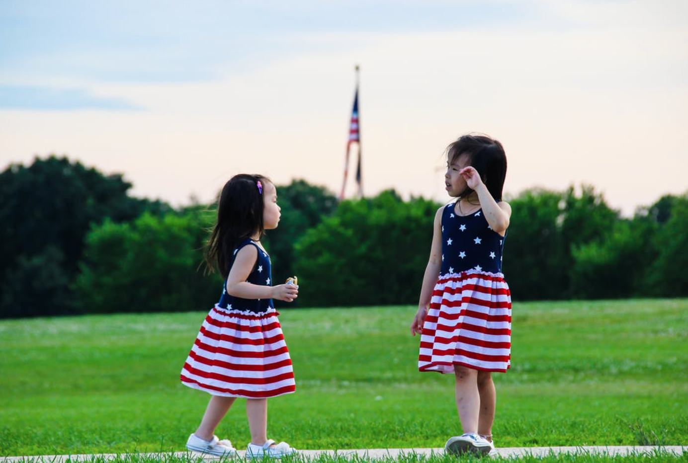 Little girls in American flag dresses standing on the lawn; image by Ahmet Bozkuş, via Pexels.com.