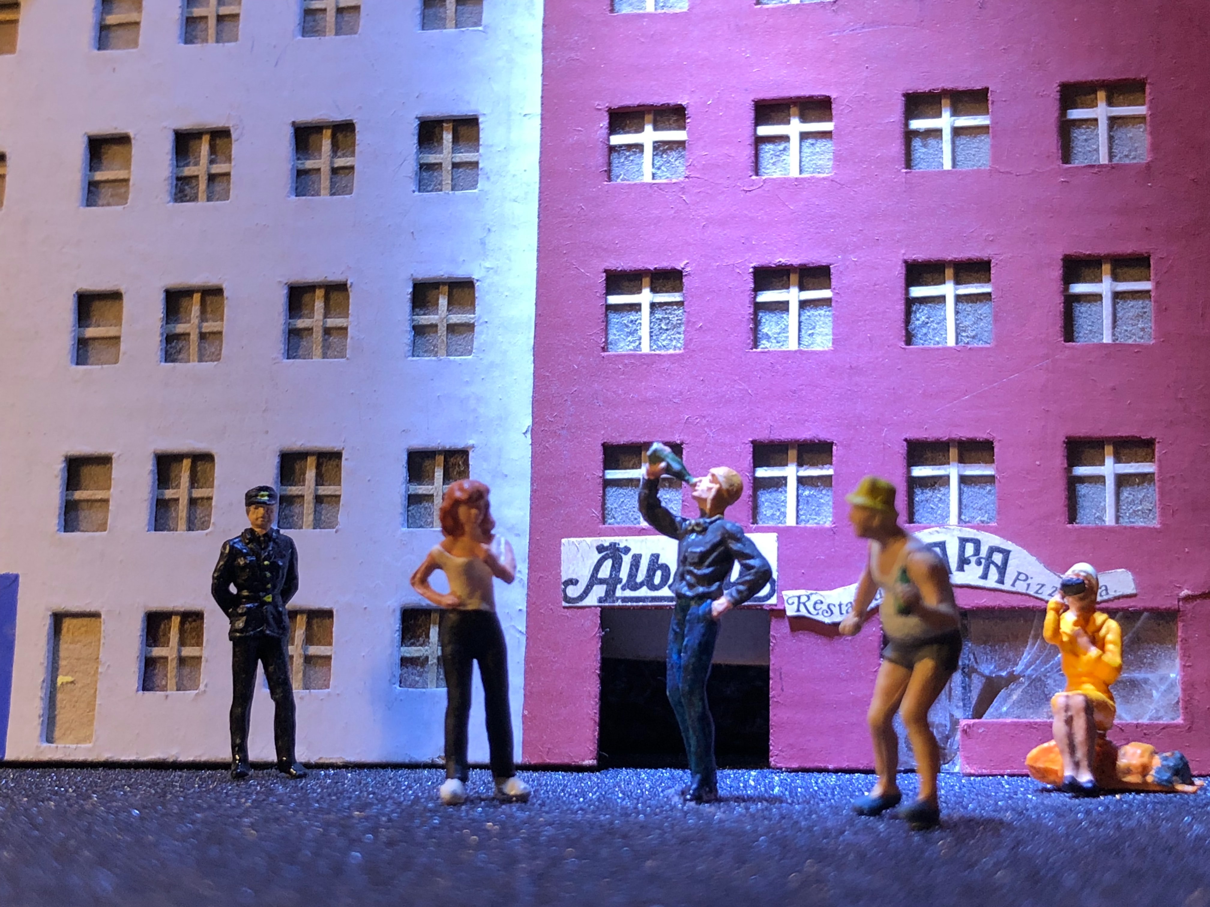 Plastic figures in front of buliding mock-up, one drinking from bottle; image by Claus Jensen, via Unsplash.com.