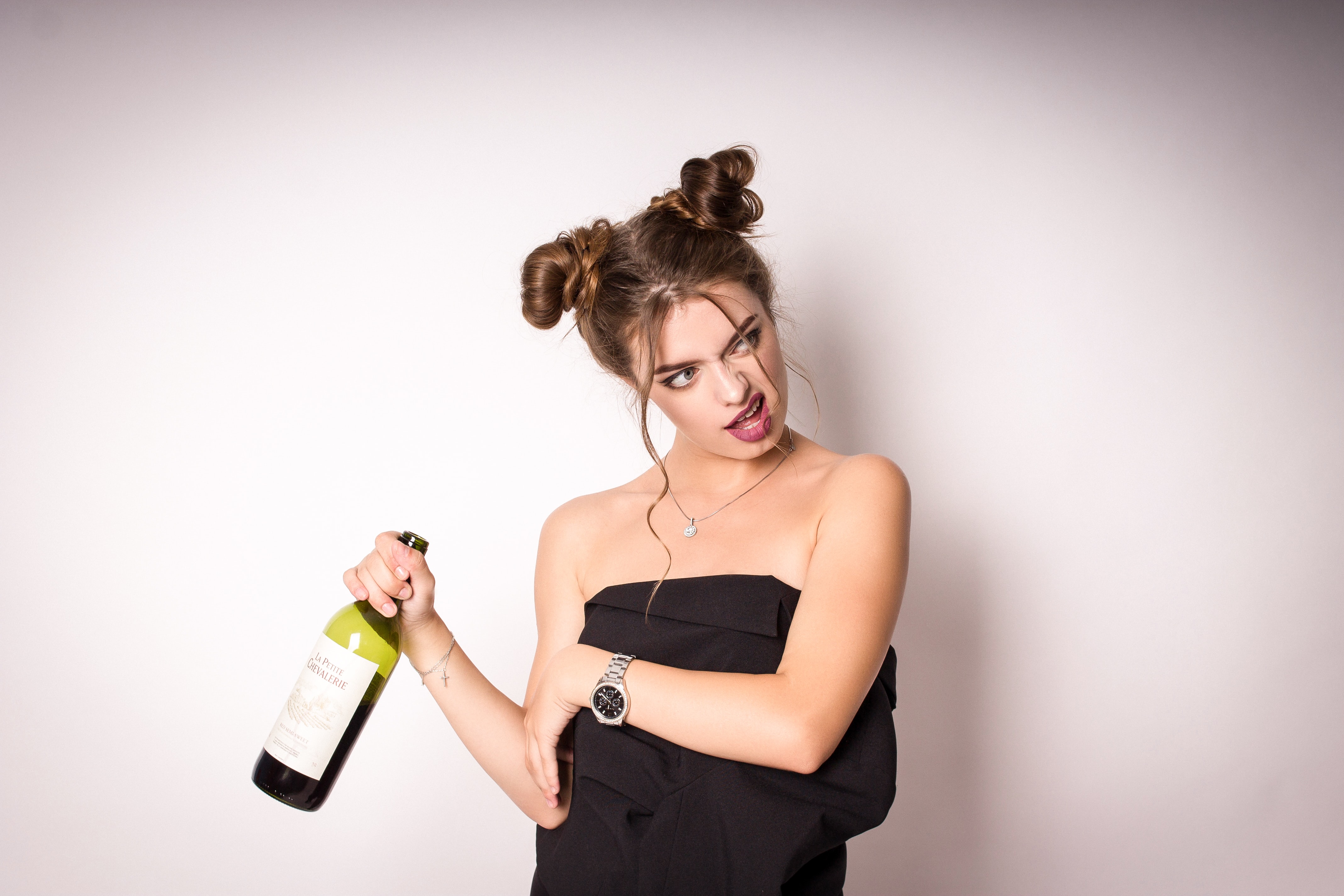 Woman in black dress with wine bottle and funny expression; image by Andrey Zvyagintsev, via Unsplash.com.
