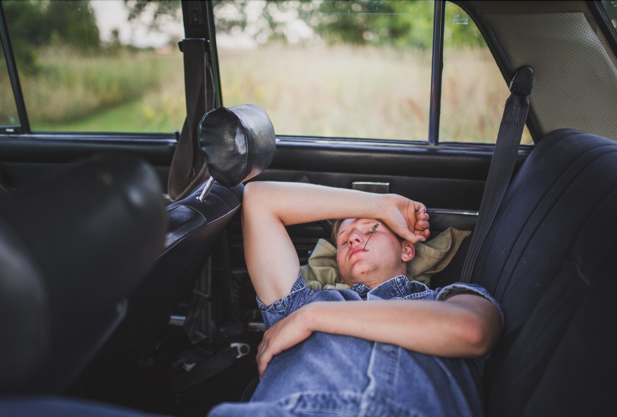 Young man sleeping in back of car; image by Elvis Bekmanis, via Unsplash.com.