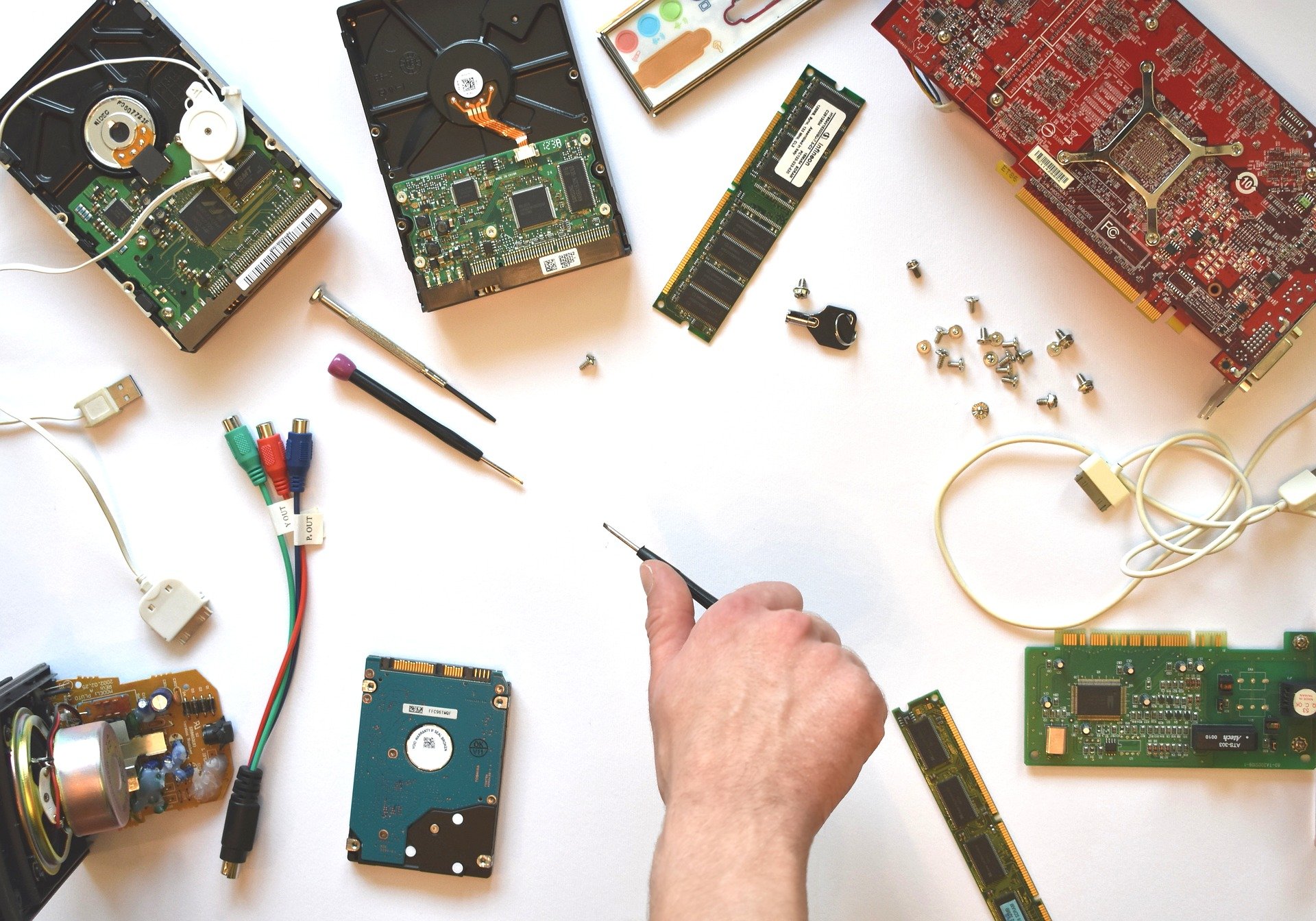 A hand holds a tool, surrounded by an array of loose computer parts and components.