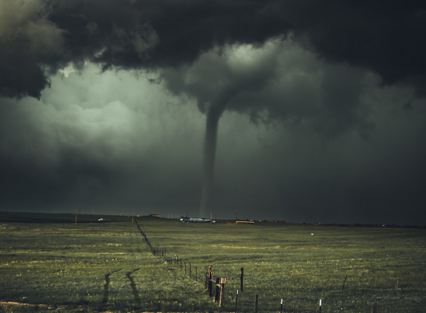 Thick, menacing clouds and a distant tornado dominate a rural landscape.