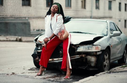 Woman in red pants and white top sitting on wrecked car; image by Godisable Jacob, via Pexels.com.