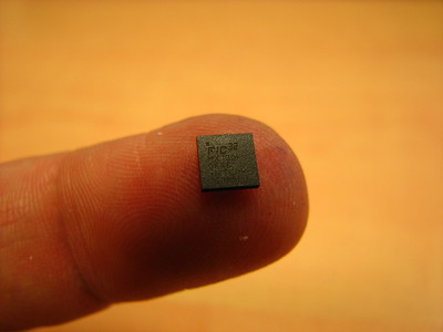 An older computer chip, smaller than the fingertip it rests upon.