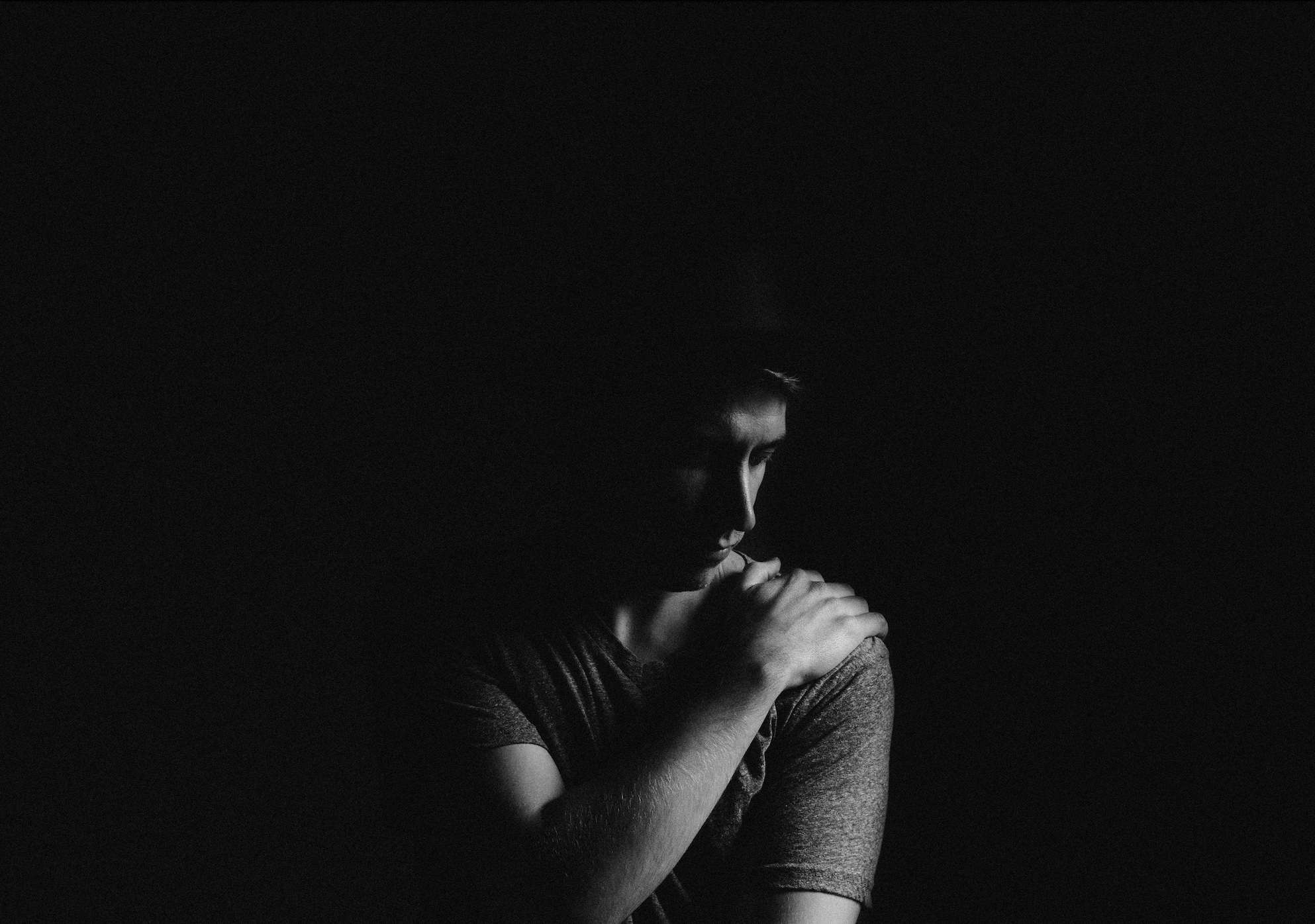 Black and white shot of man holding his left shoulder; image by Mitchell Hollander, via Unsplash.com.