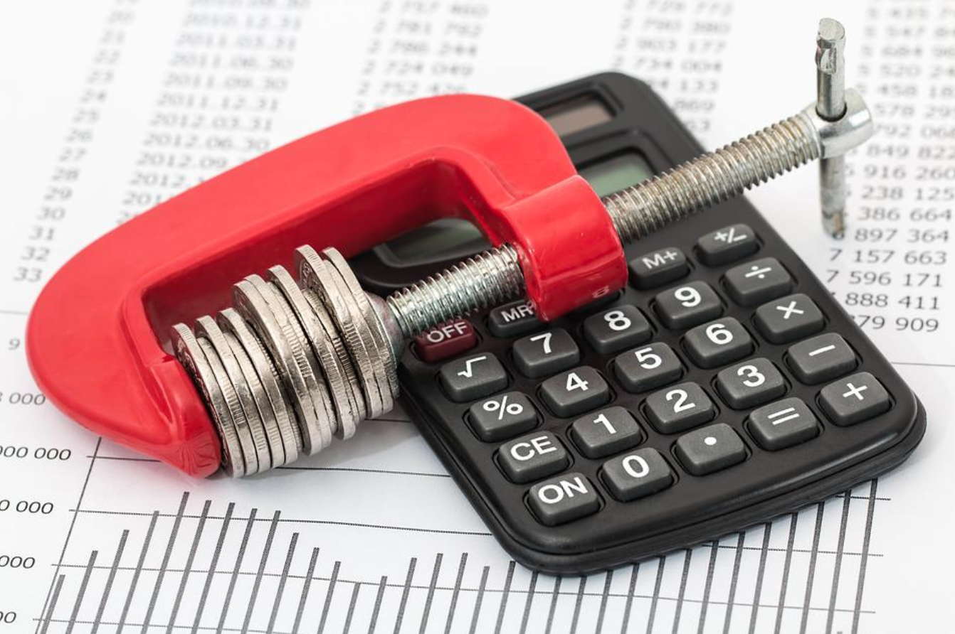 Budget paper with a calculator and a clamp holding coins; image by Stevepb, via Pixabay.com.