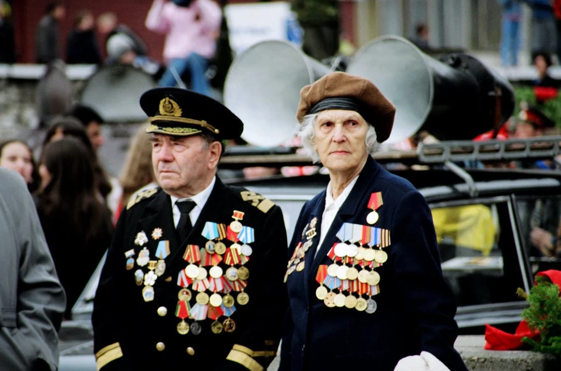 Elderly woman and man wearing military uniforms; image by Carmen Attal, via Pexels.com.