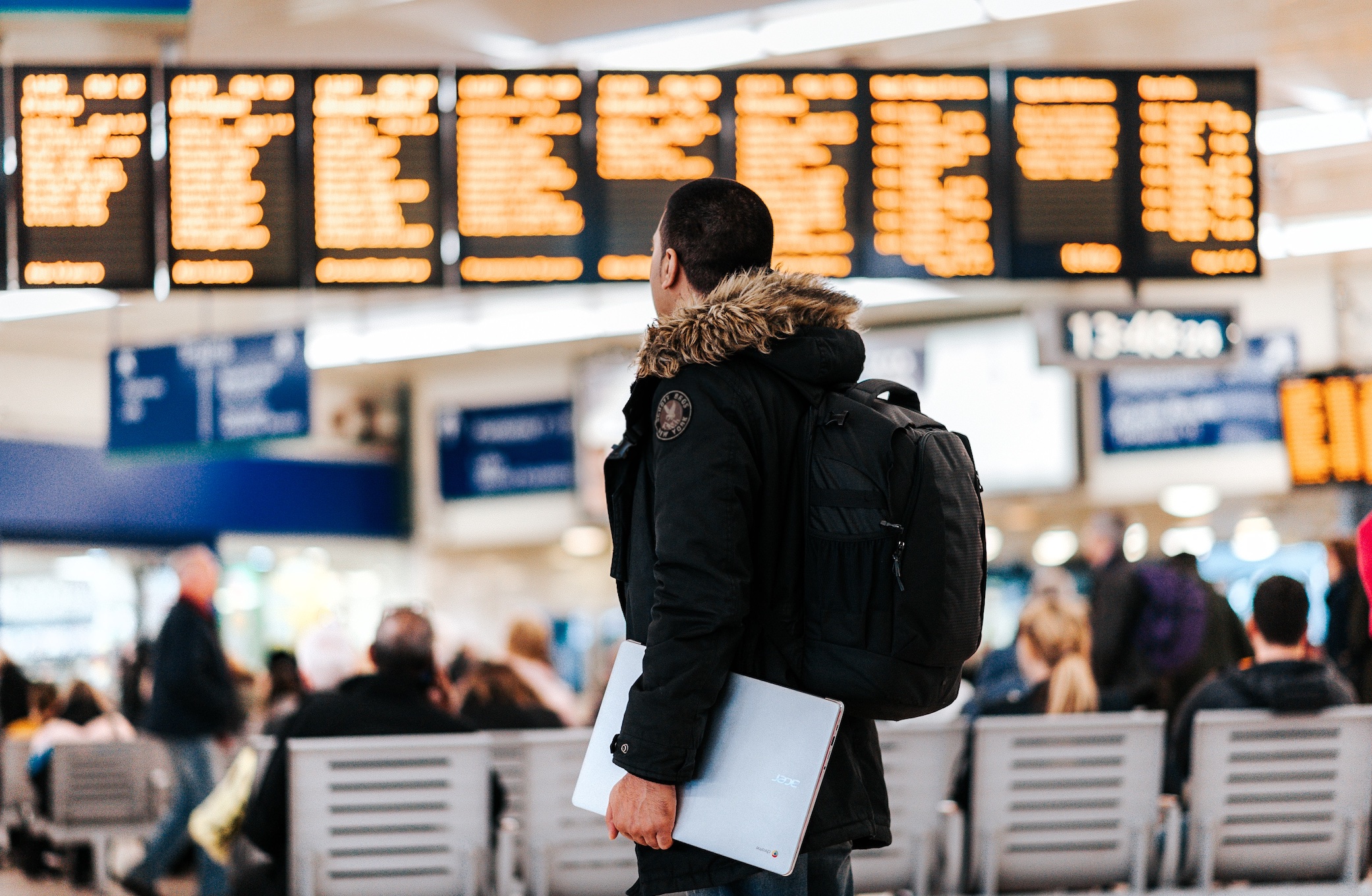 Man in airport looking at flight schedules; image by Anete Lusina, via Unsplash.com.