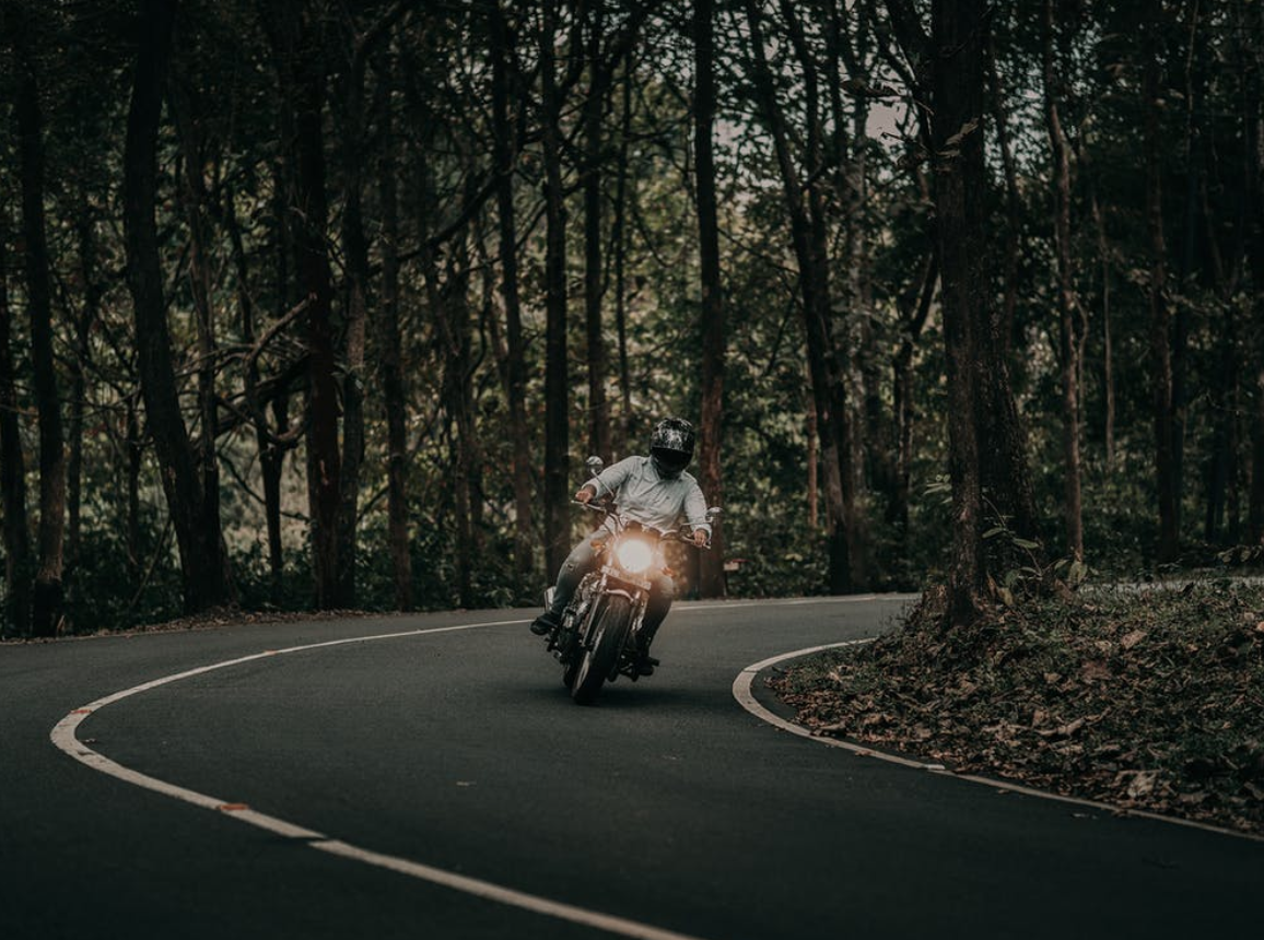 Man riding motorcycle around a curve; image by Nandu Vasudevan, via Pexels.com.