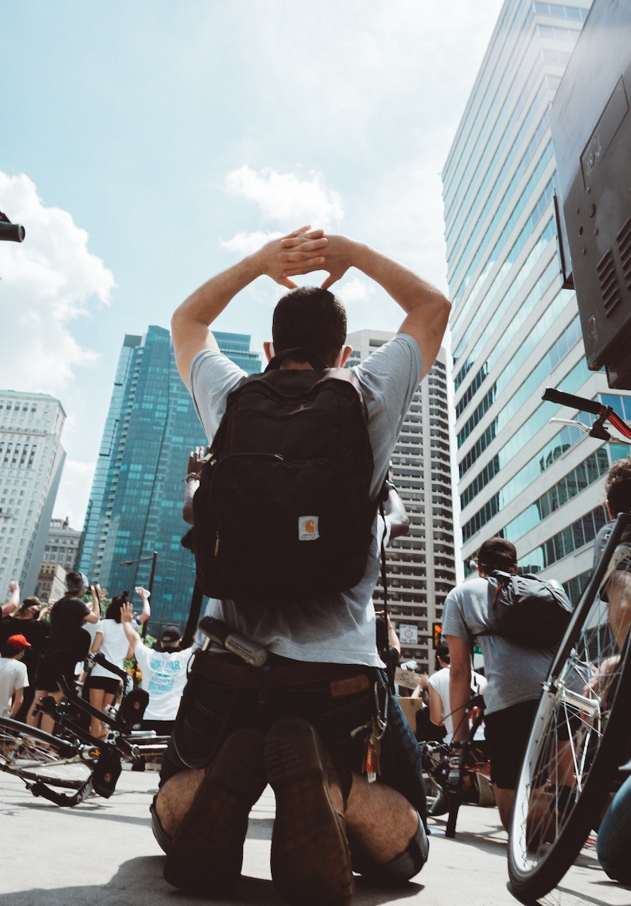 Man with backpack on knees with hands in the air; image by Chris Henry, via Unsplash.com.