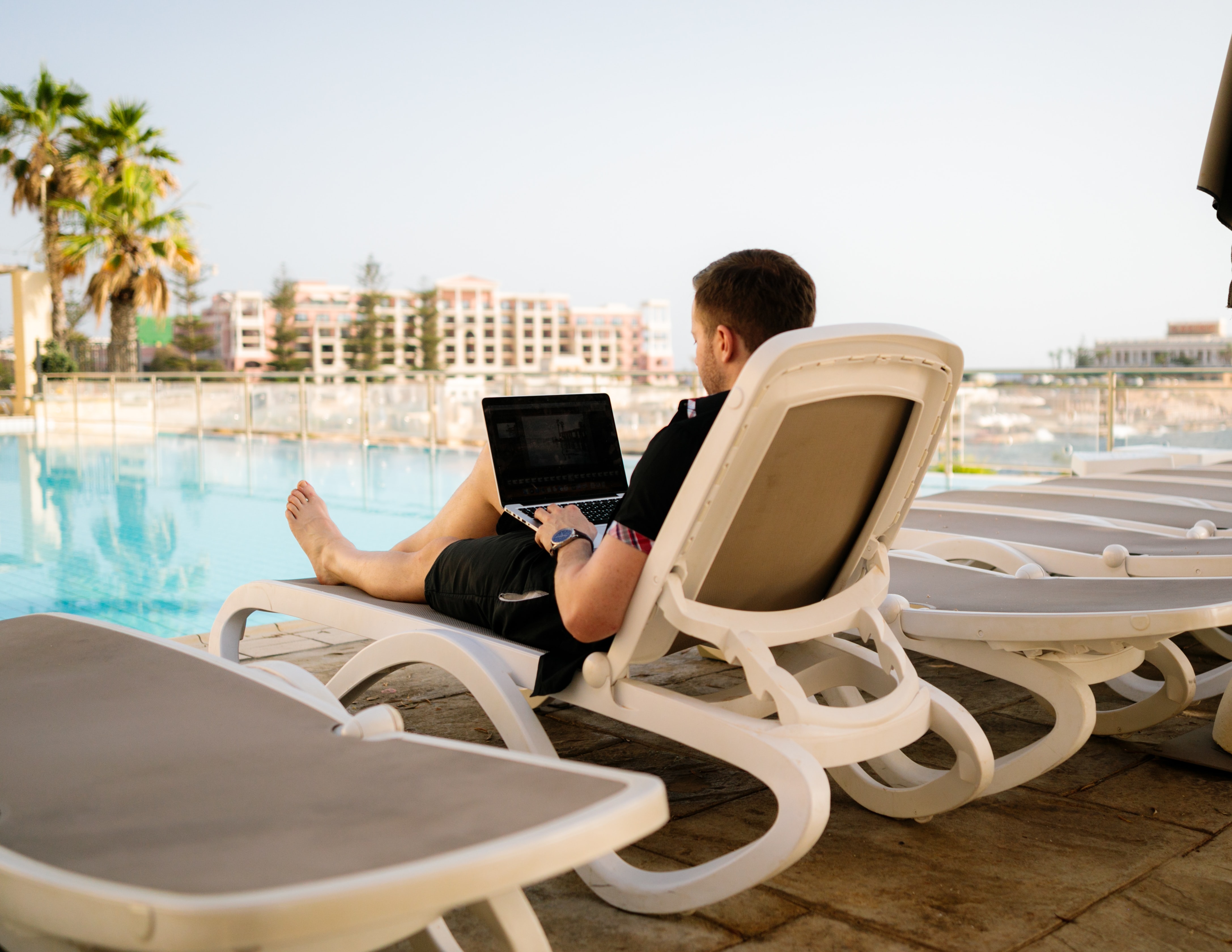 Life of a digital nomad, work and travel lifestyle. Man on sun lounger using laptop. Image by Humphrey Muleba, via Unsplash.com.