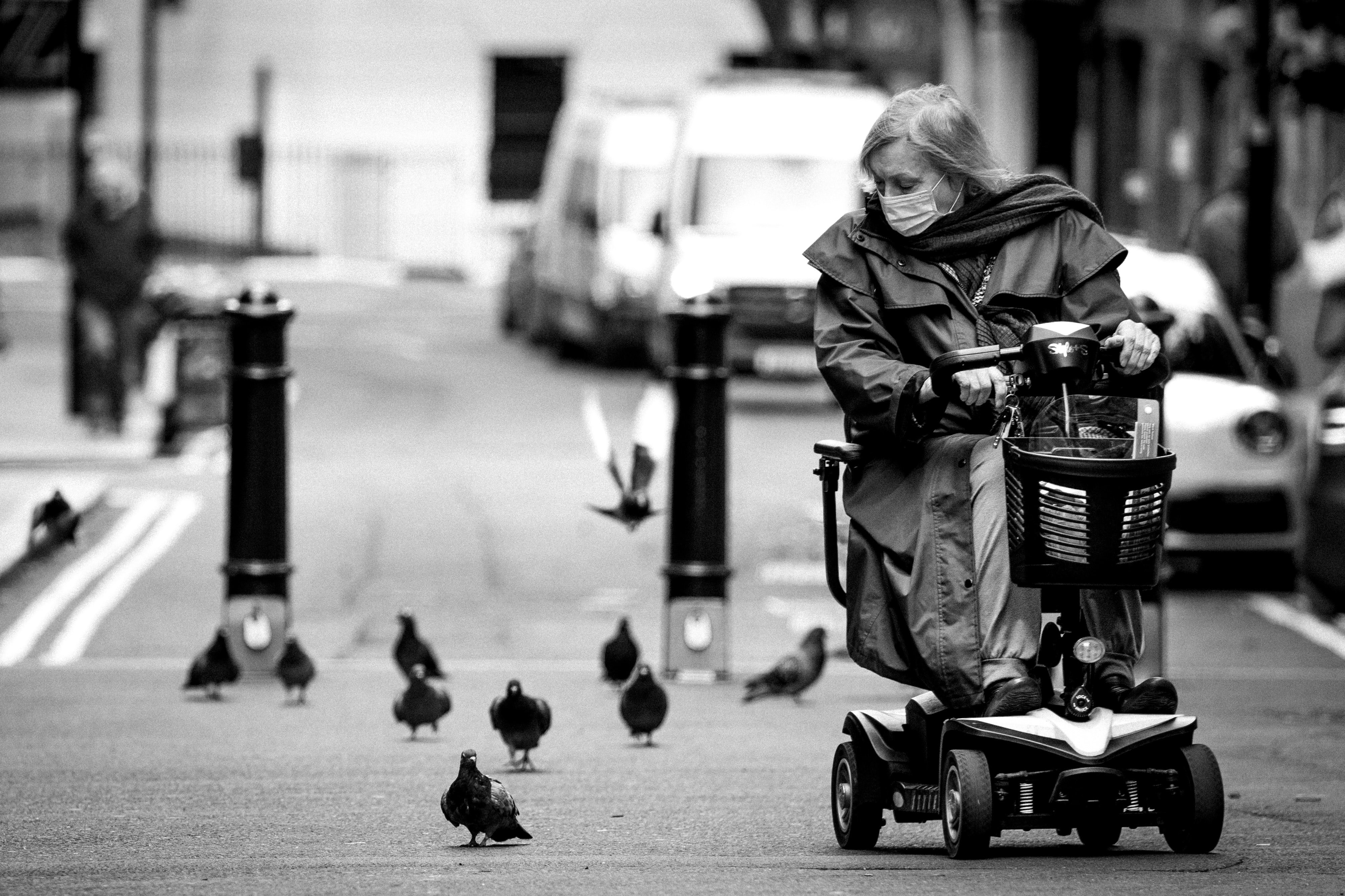 Black and white image of woman on mobility scooter looking a birds; image by Ben Wicks, via Unsplash.com.