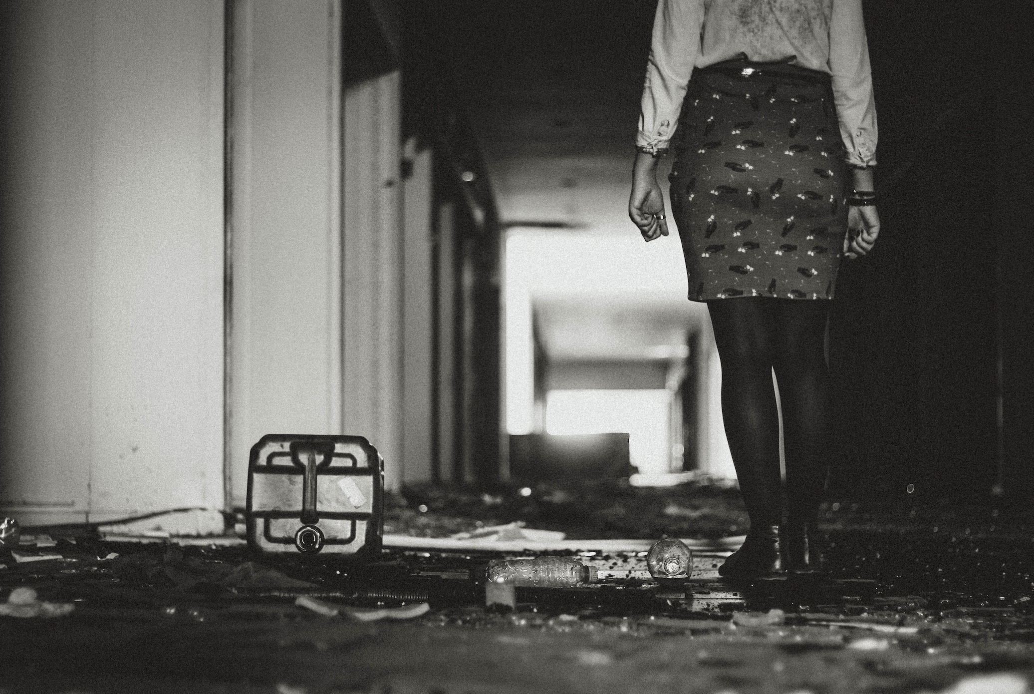 Black and white photo of woman in skirt standing in water damaged building; image by Allef Vinicius, via Unsplash.com.
