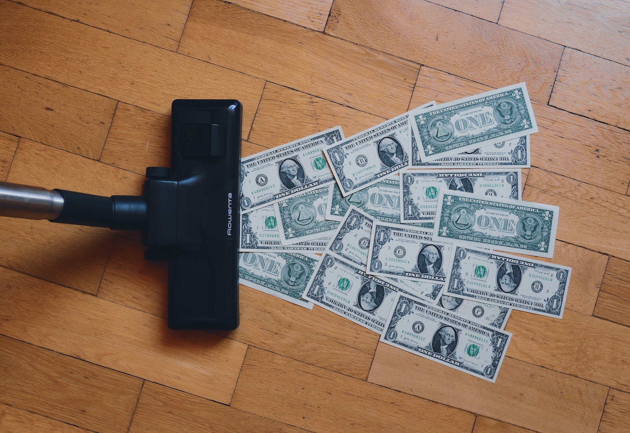 Vacuum cleaner sucking up dollar bills; image by RegularGuy.eth, via Unsplash.com.