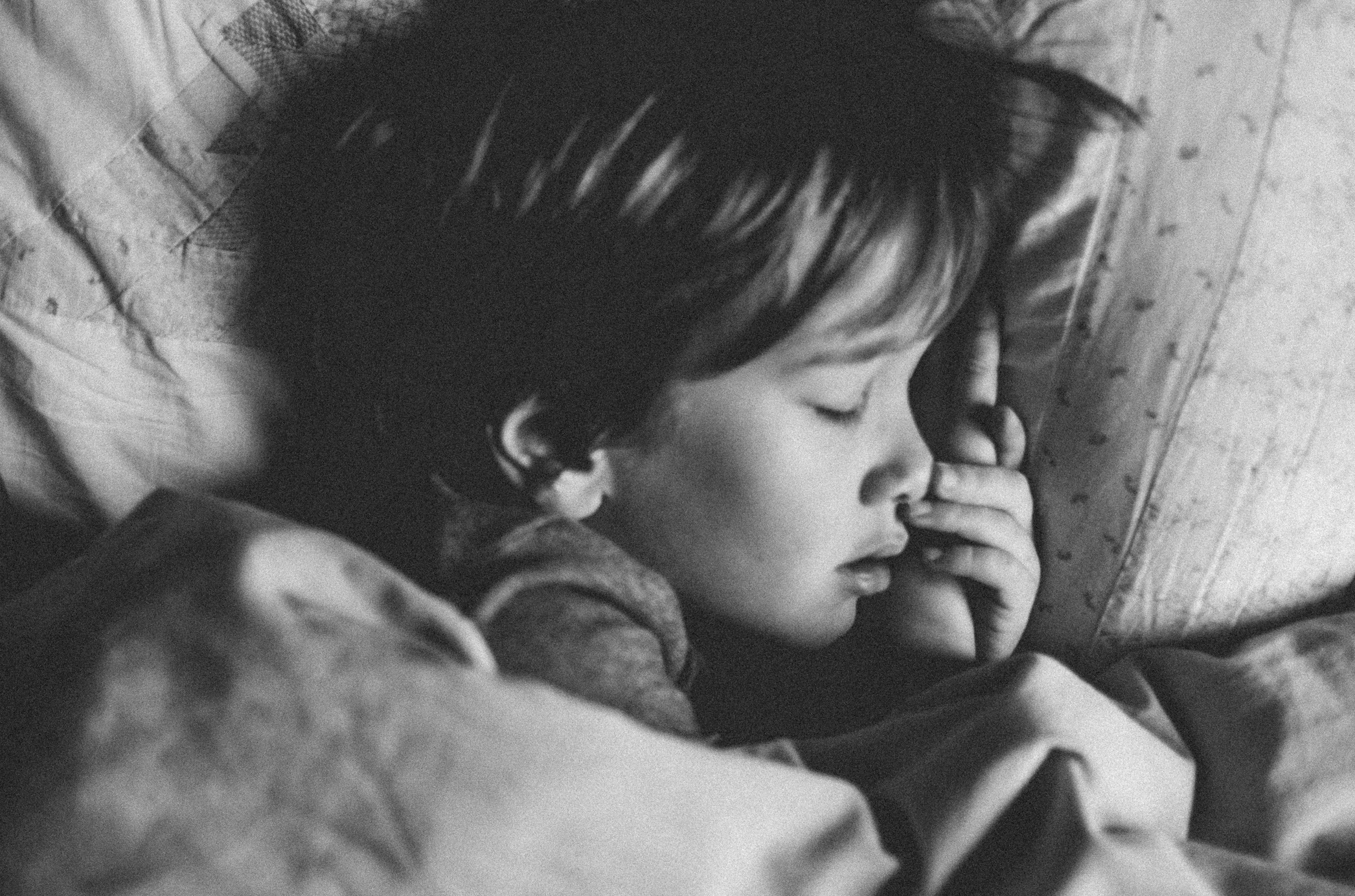 Black and white photo of boy sleeping in bed; image by Annie Spratt, via Unsplash.com.