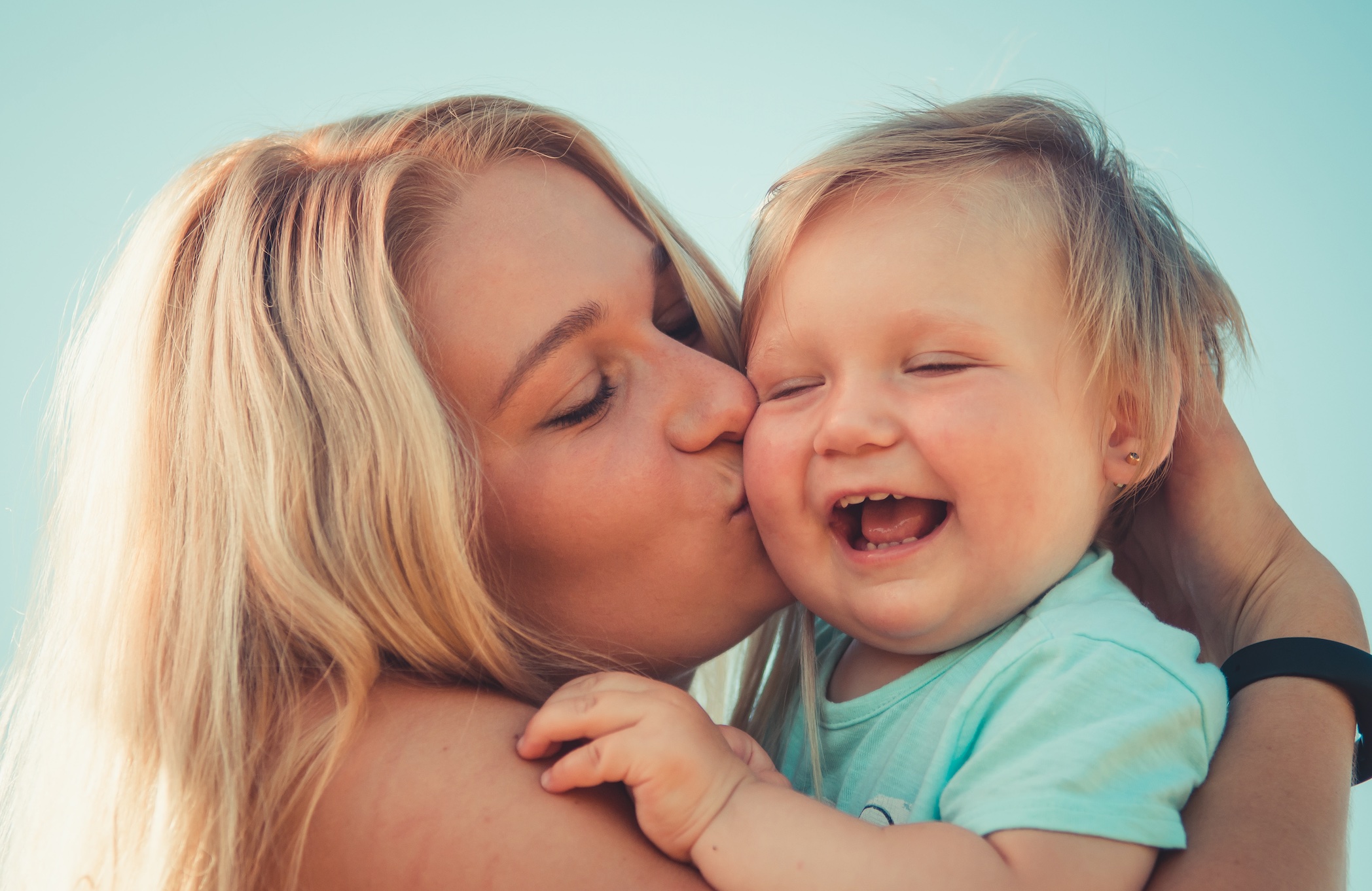 Blonde woman holding blonde girl and kissing her on the cheek; image by Andriyko Podilnyk, via Unsplash.com.