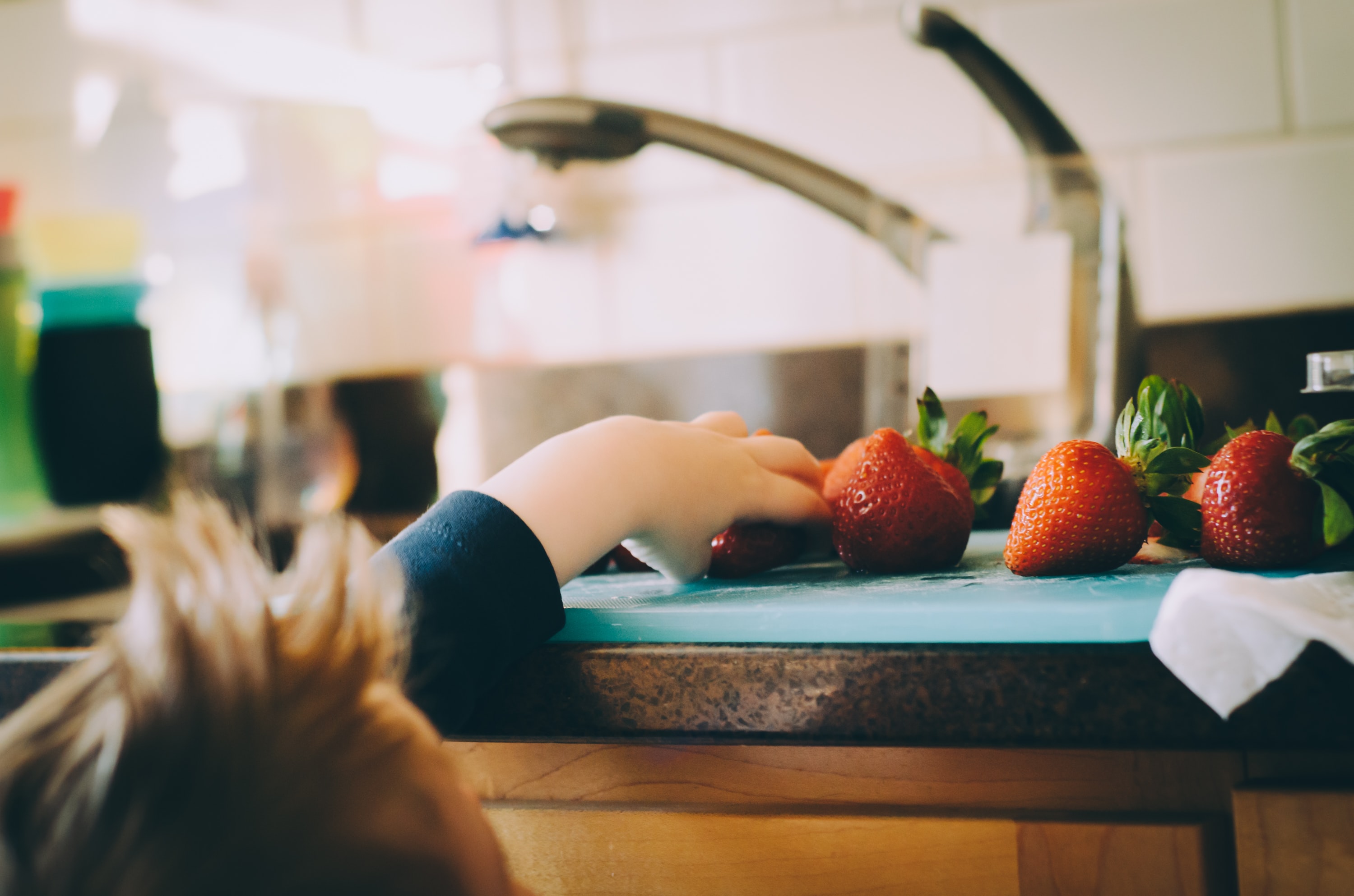 Child taking strawberry off of kitchen counter; image by Kelly Sikkema, via Unsplash.com.
