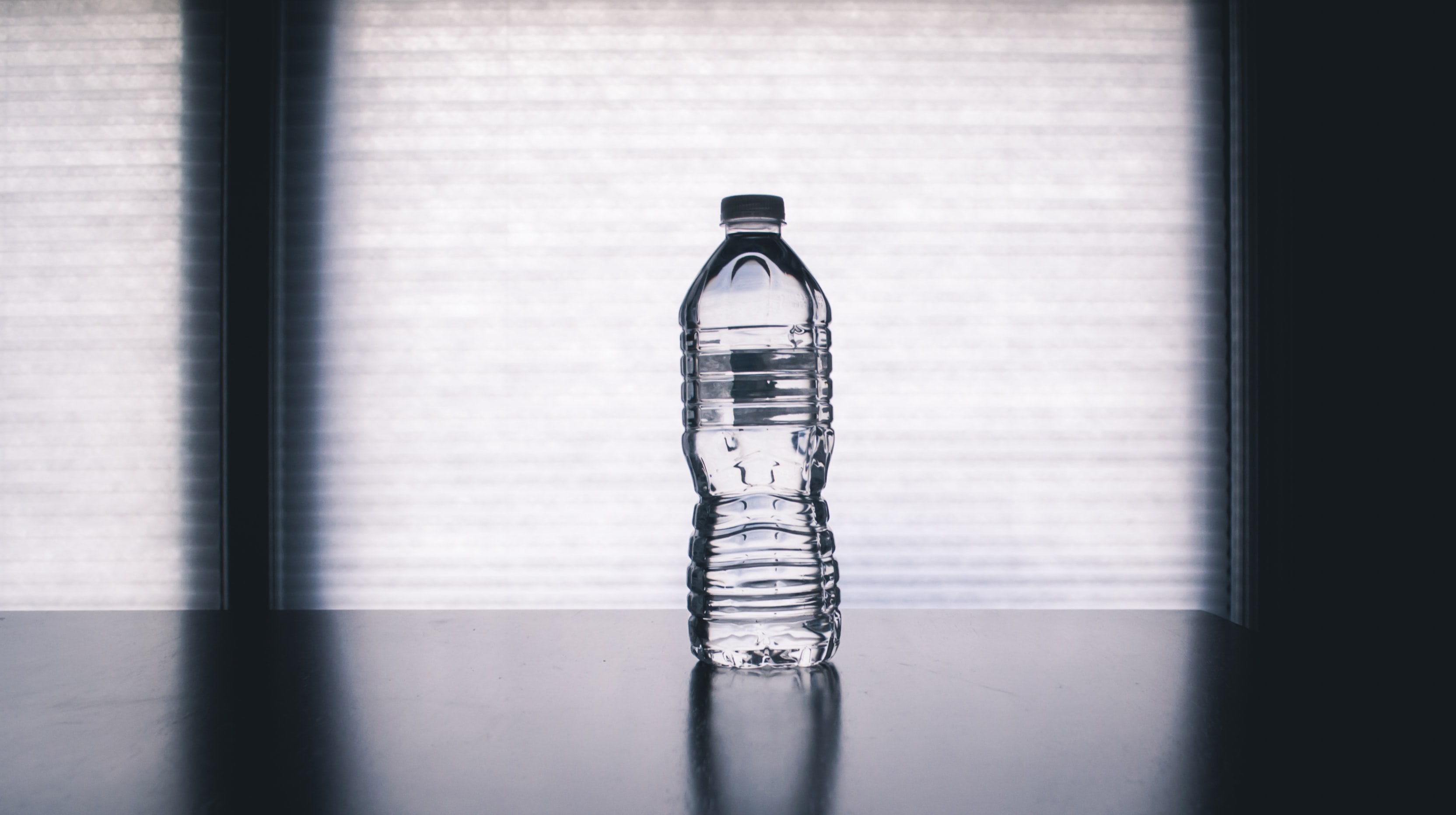 Clear plastic bottle of water on black table; image bySteve Johnson, via Unsplash.com.