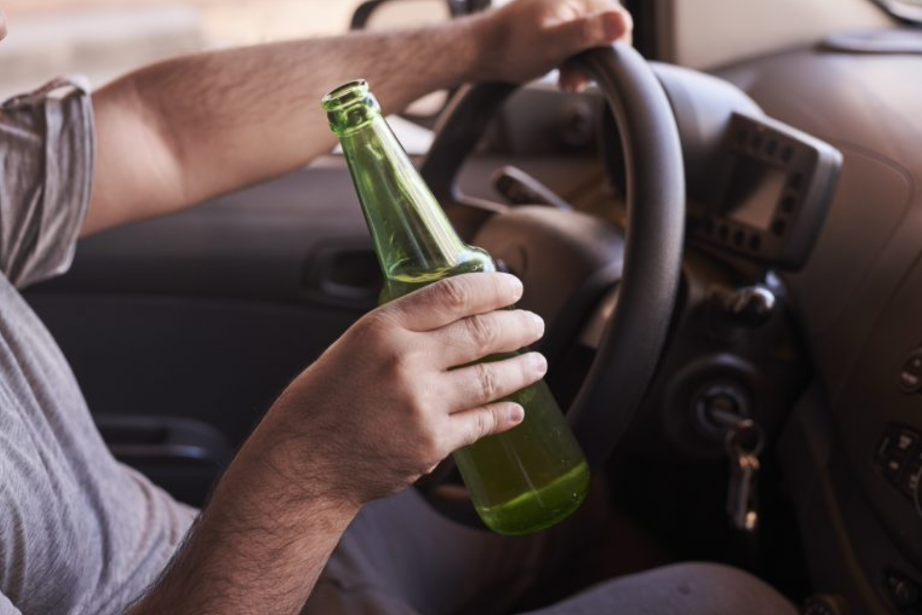 Drunk and drive. Man behind the wheel with open beer bottle; image via Imagesource.io.