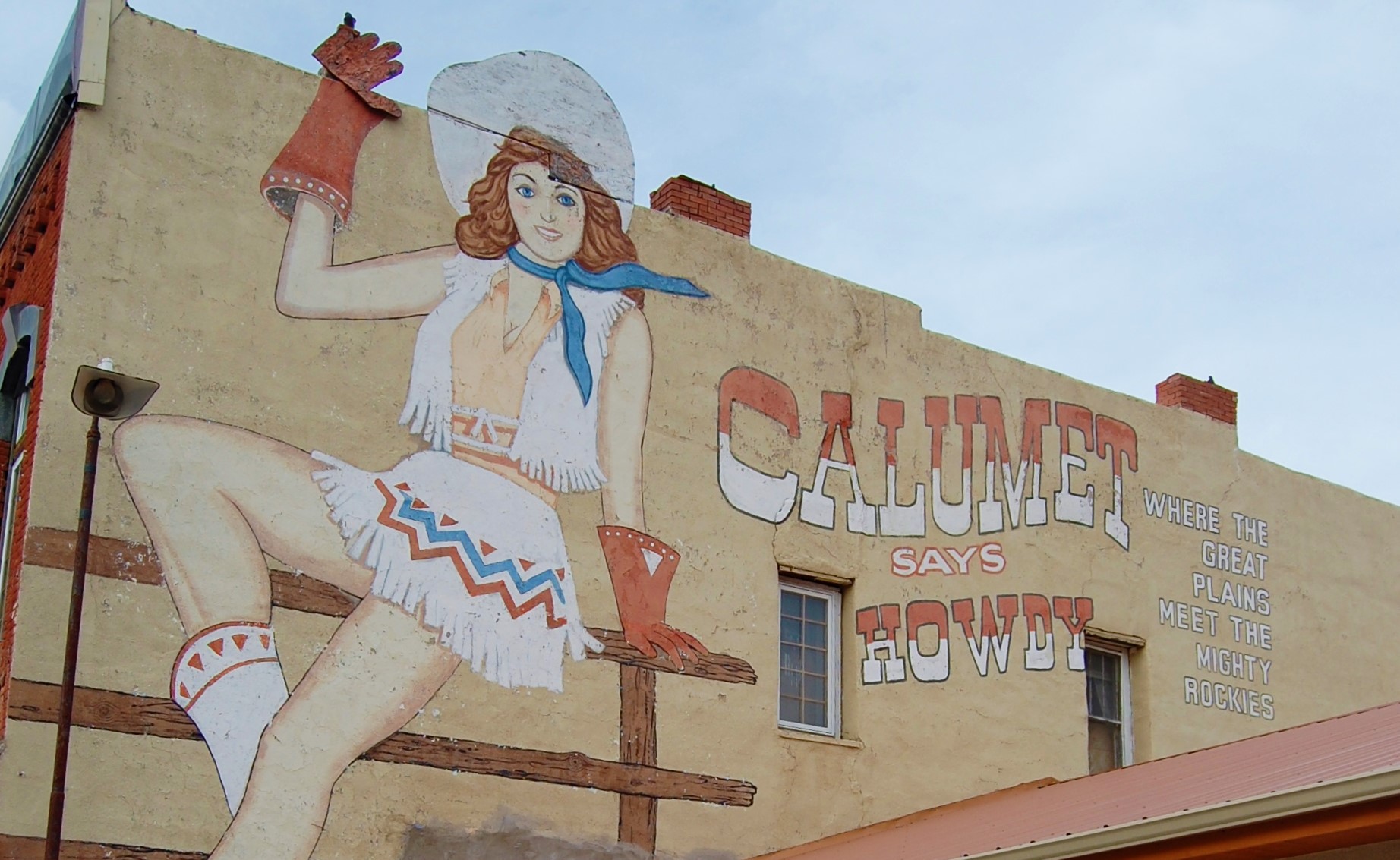 A painted mural of a woman in Western attire, on the side of a brick building.