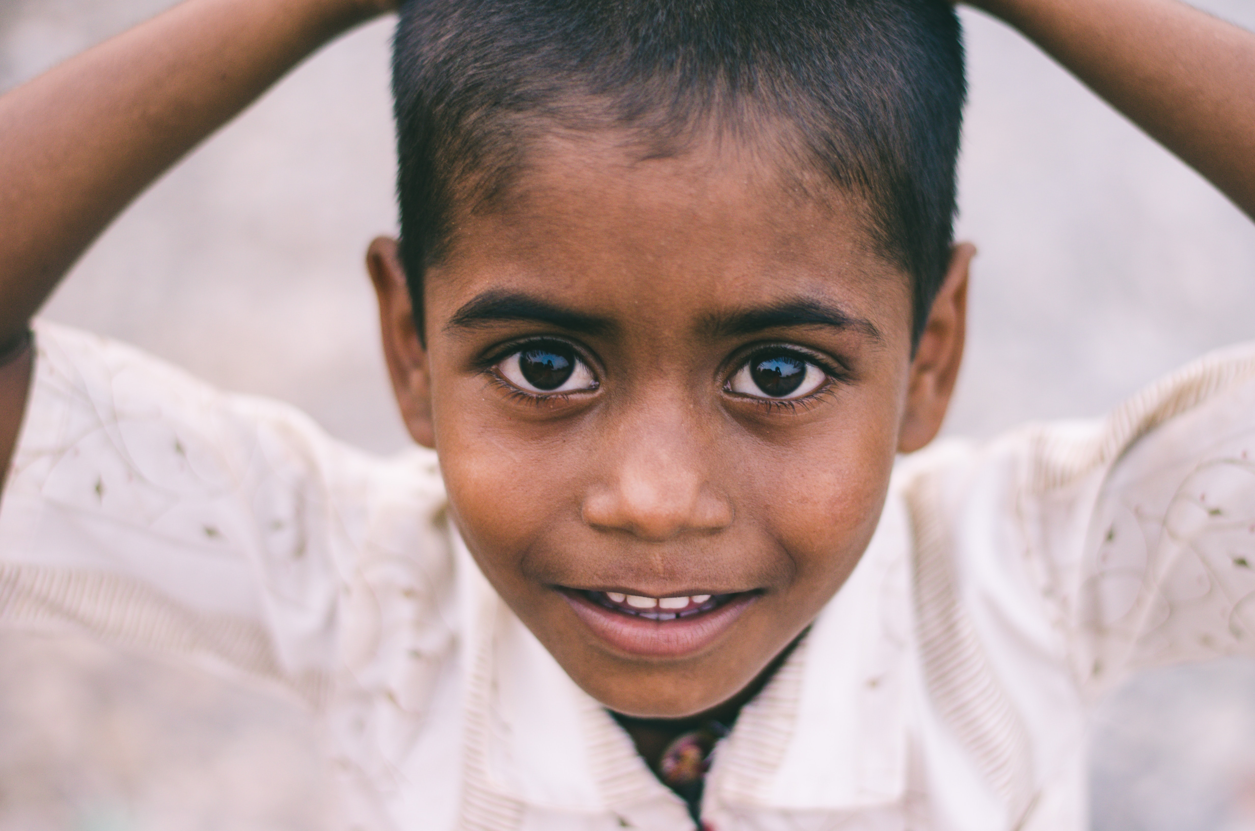 Little Indian boy with hands on head looking into camera; image by Shravan K. Acharya, via Unsplash.com.