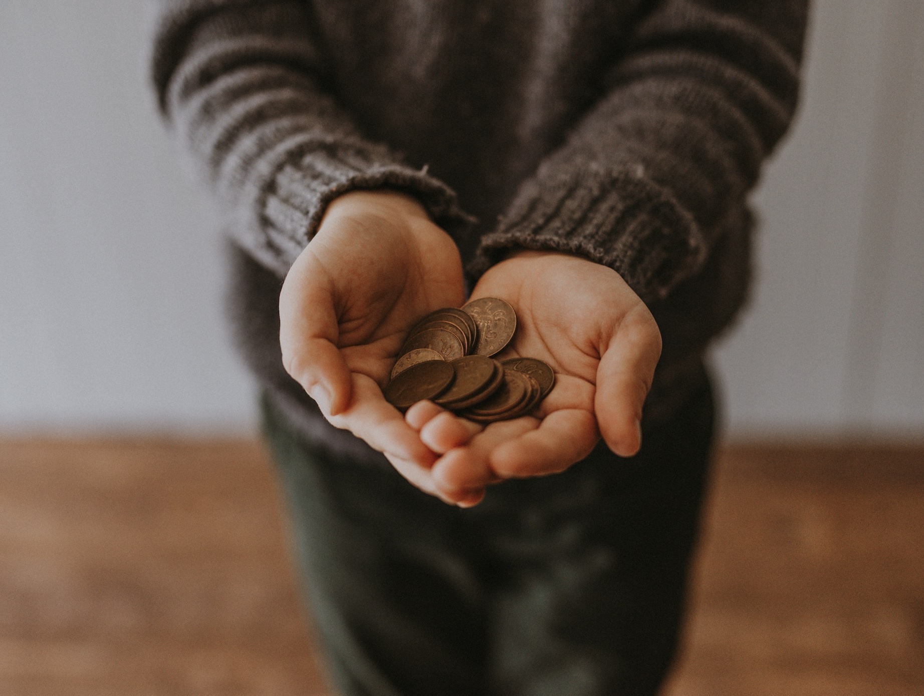 Man in brown sweater holding out hands with coins; image by Annie Spratt, via Unsplash.com.