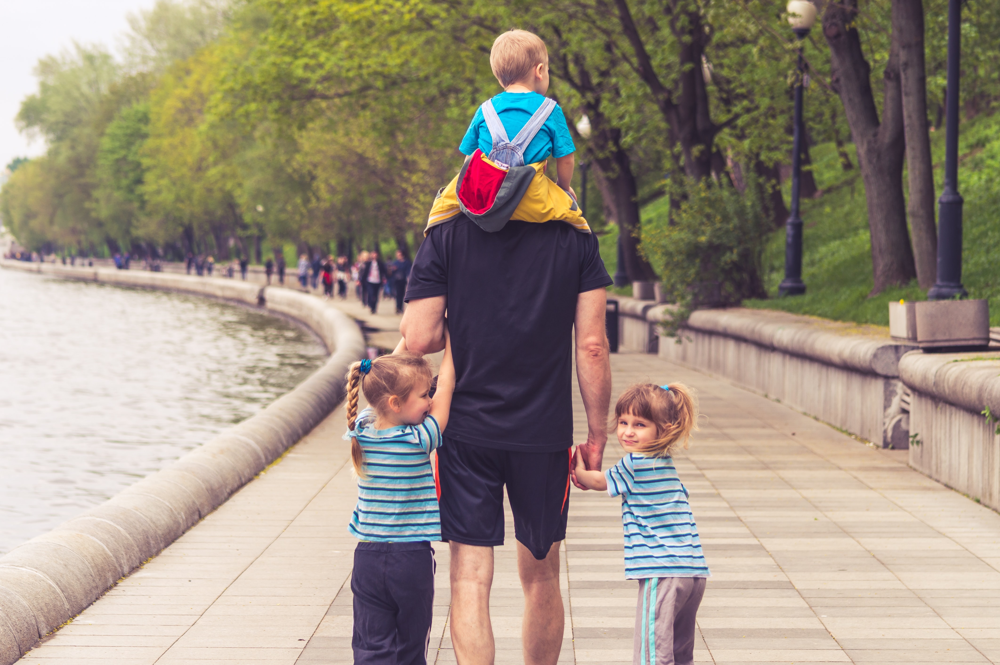 Man walking away from camera holding hands with two little girls and carrying little boy on his shoulders; image by Vitolda Klein, via Unsplash.com.