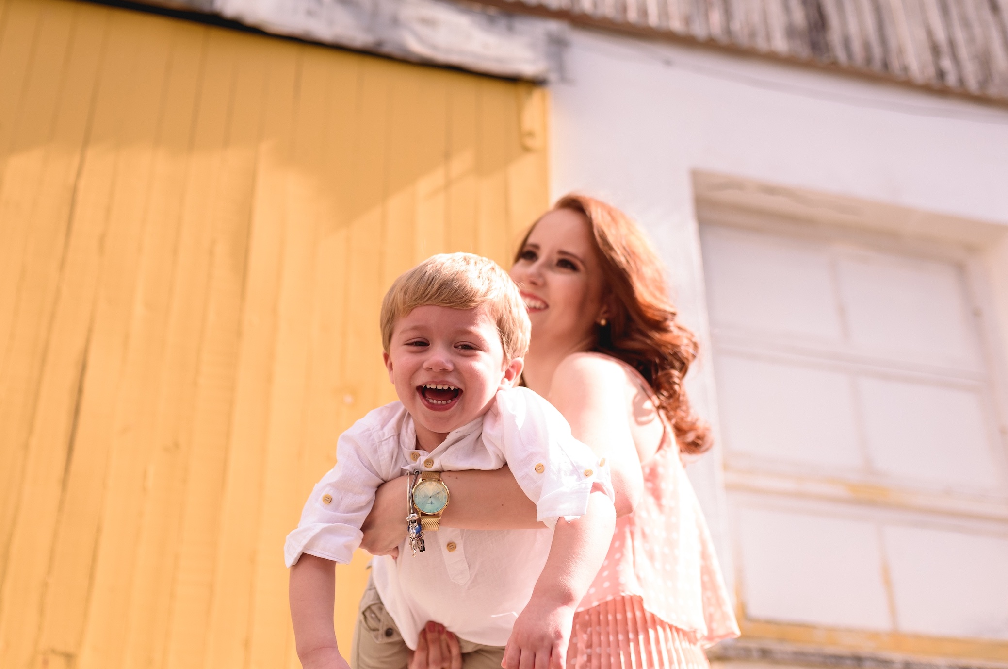 Smiling redheaded woman holding smiling blonde toddler boy; image by Fernanda Greppe, via Unsplash.com.